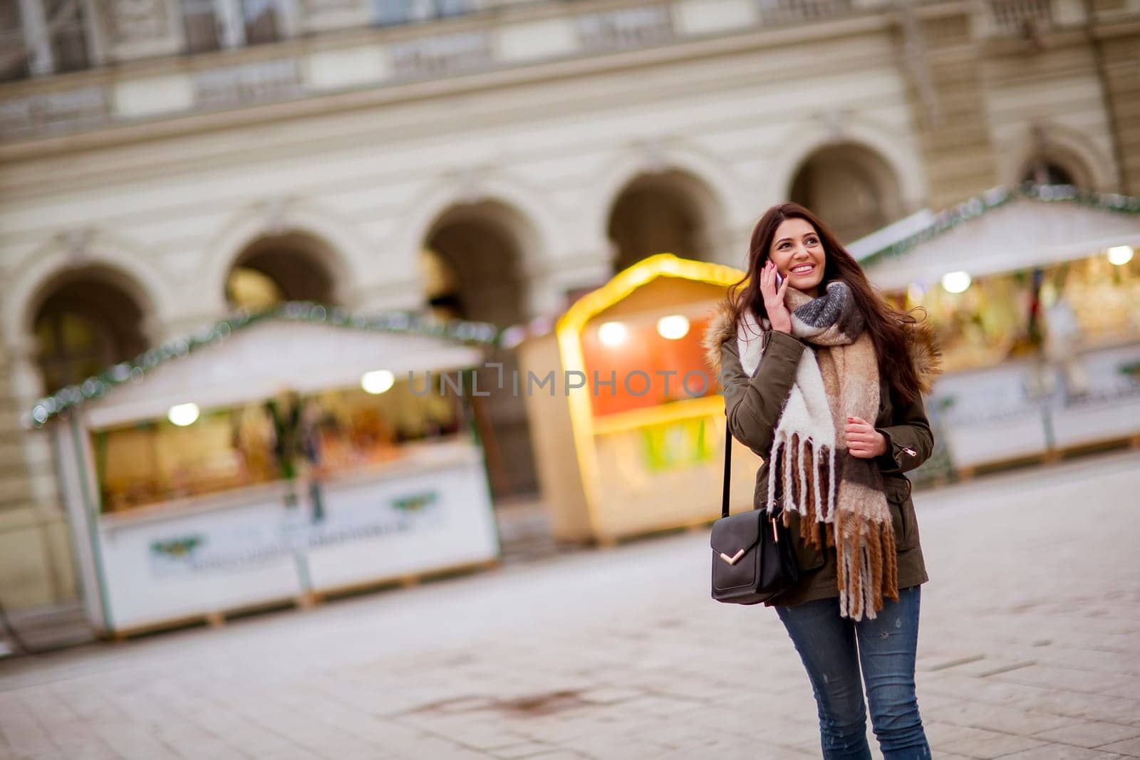 Portrait of smiling young woman using phoneon street at cold winter day at Christmas market
