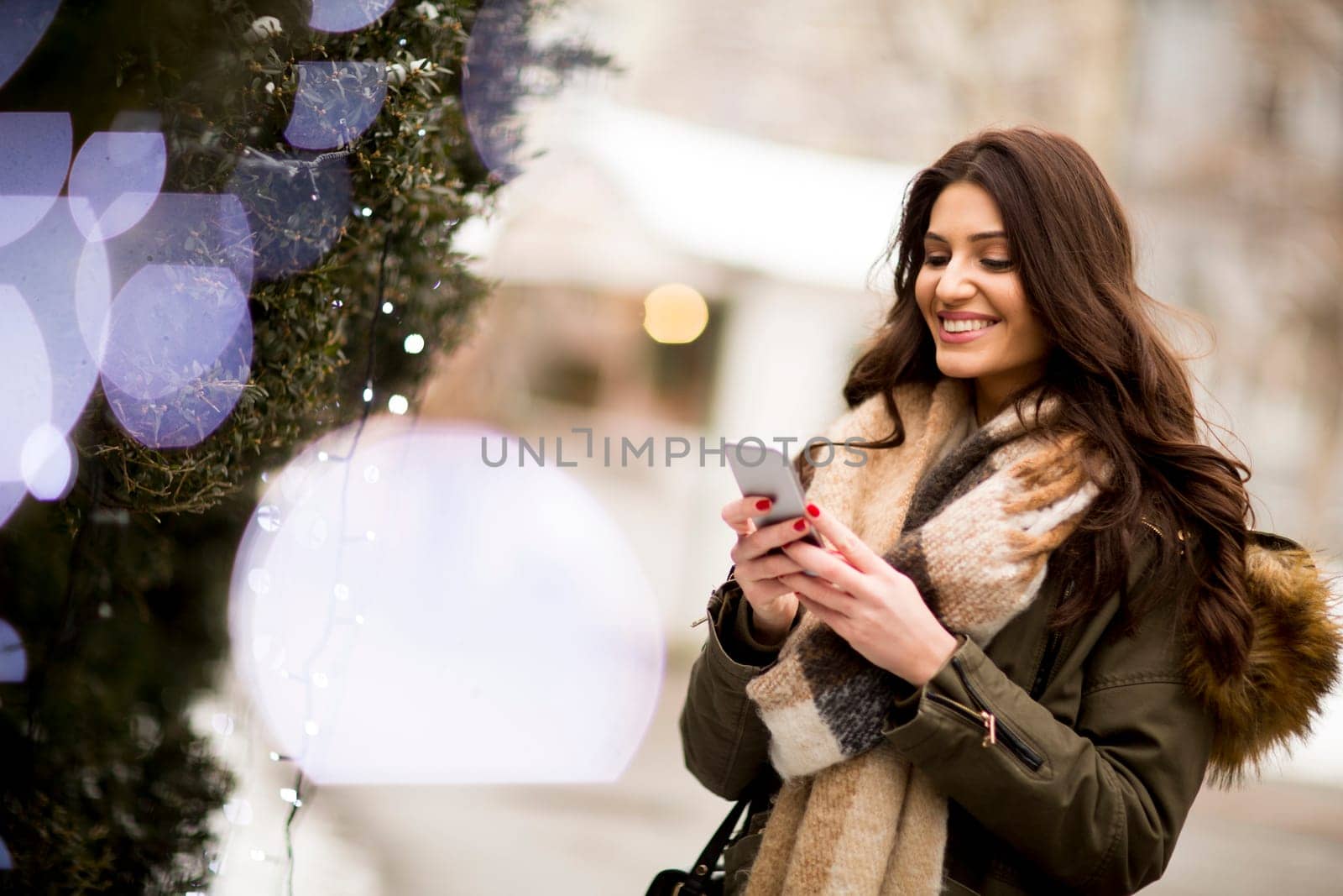 Young woman using a phone in the winter park at Christmas market