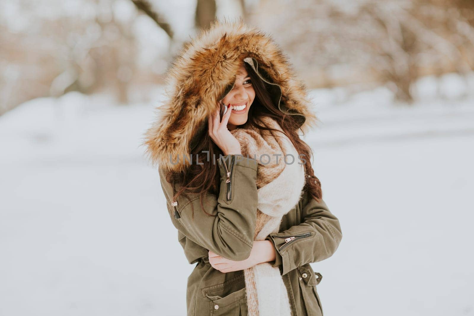 Smiling young woman using phone in park at cold winter day