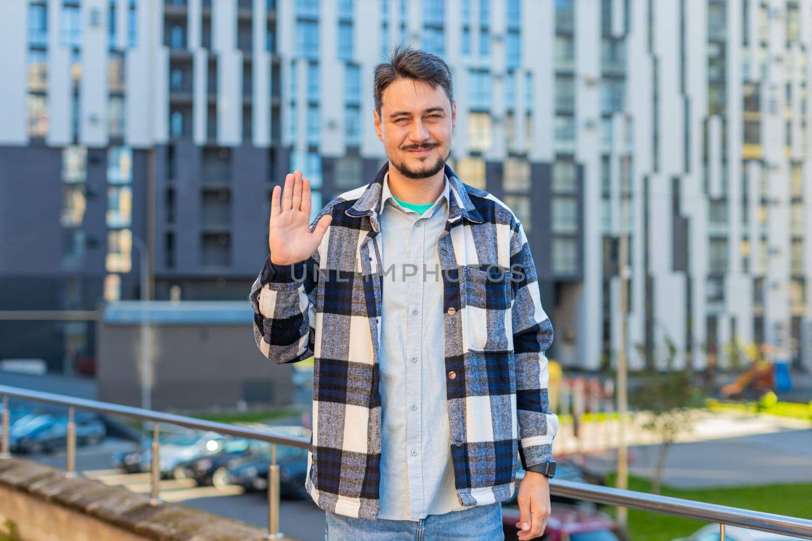 Cheerful mature man tourist smiling friendly at camera, waving hands gesturing invitation hello, hi, greeting, goodbye, welcoming with hospitable expression outdoors. Happy guy on downtown city street