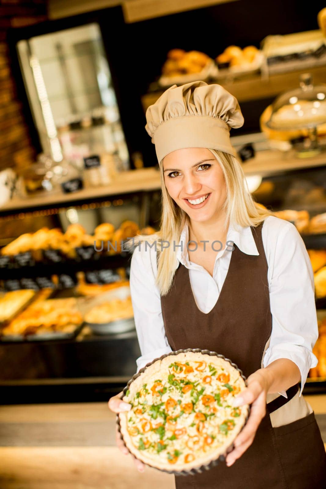 Bakery female worker posing with pizza in bakery