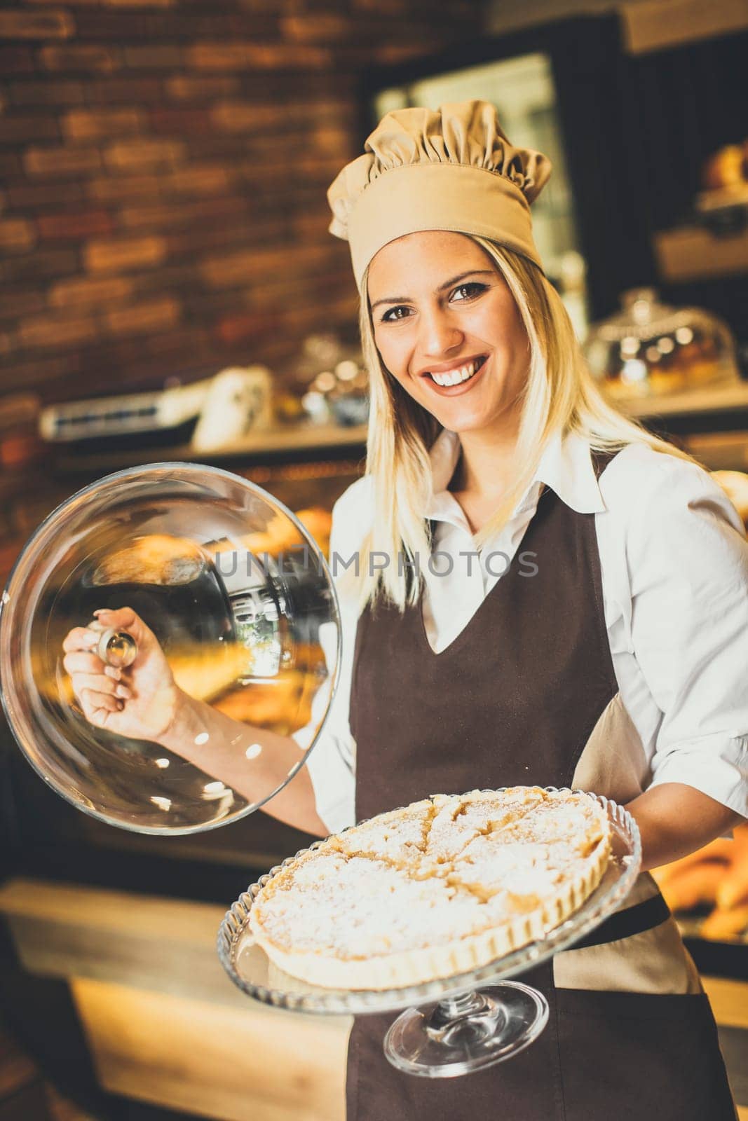 Bakery female worker posing with apple tart in baker shop