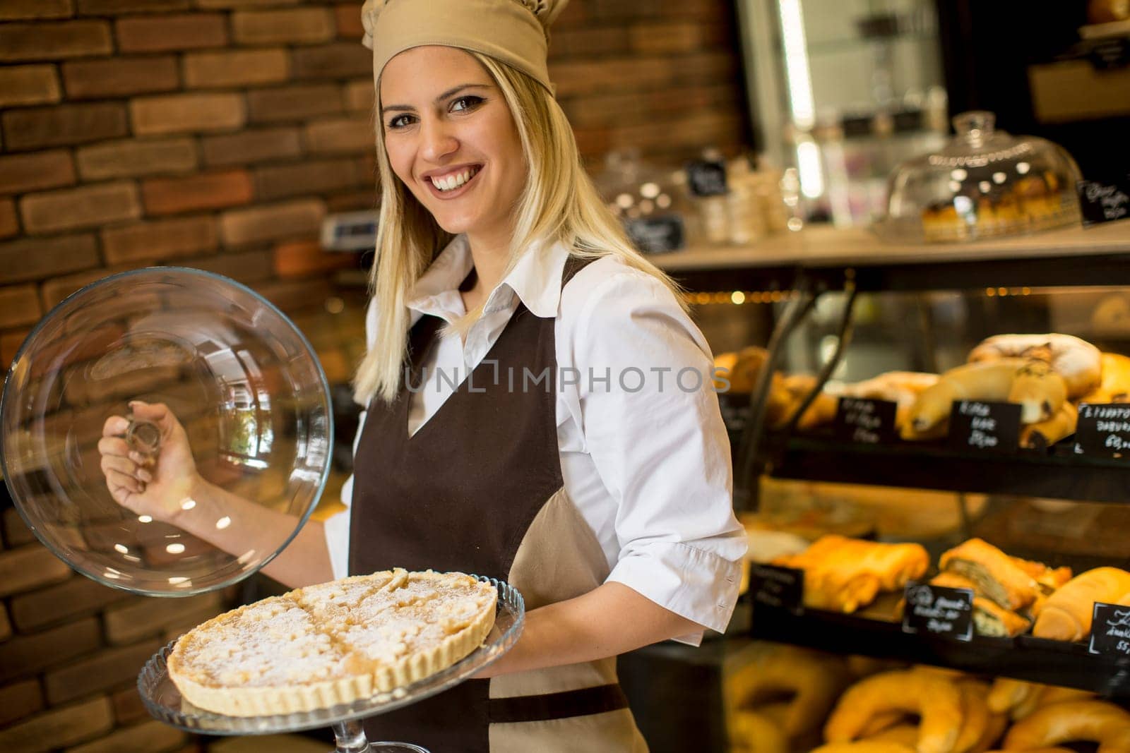 Portrait of female bakery worker posing with apple tart in baker shop