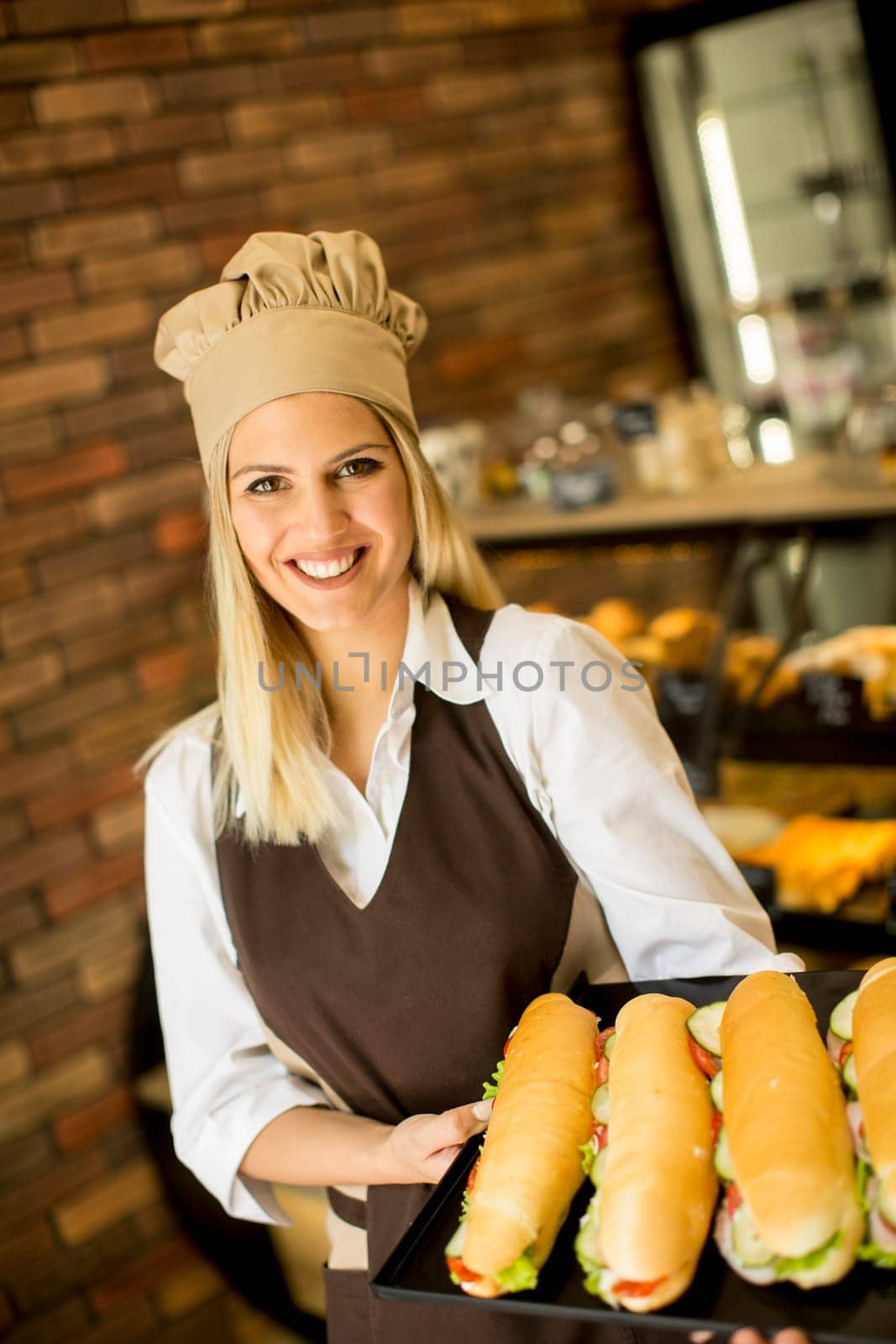 Portrait of female baker posing with various types of sandwiches in the baker shop