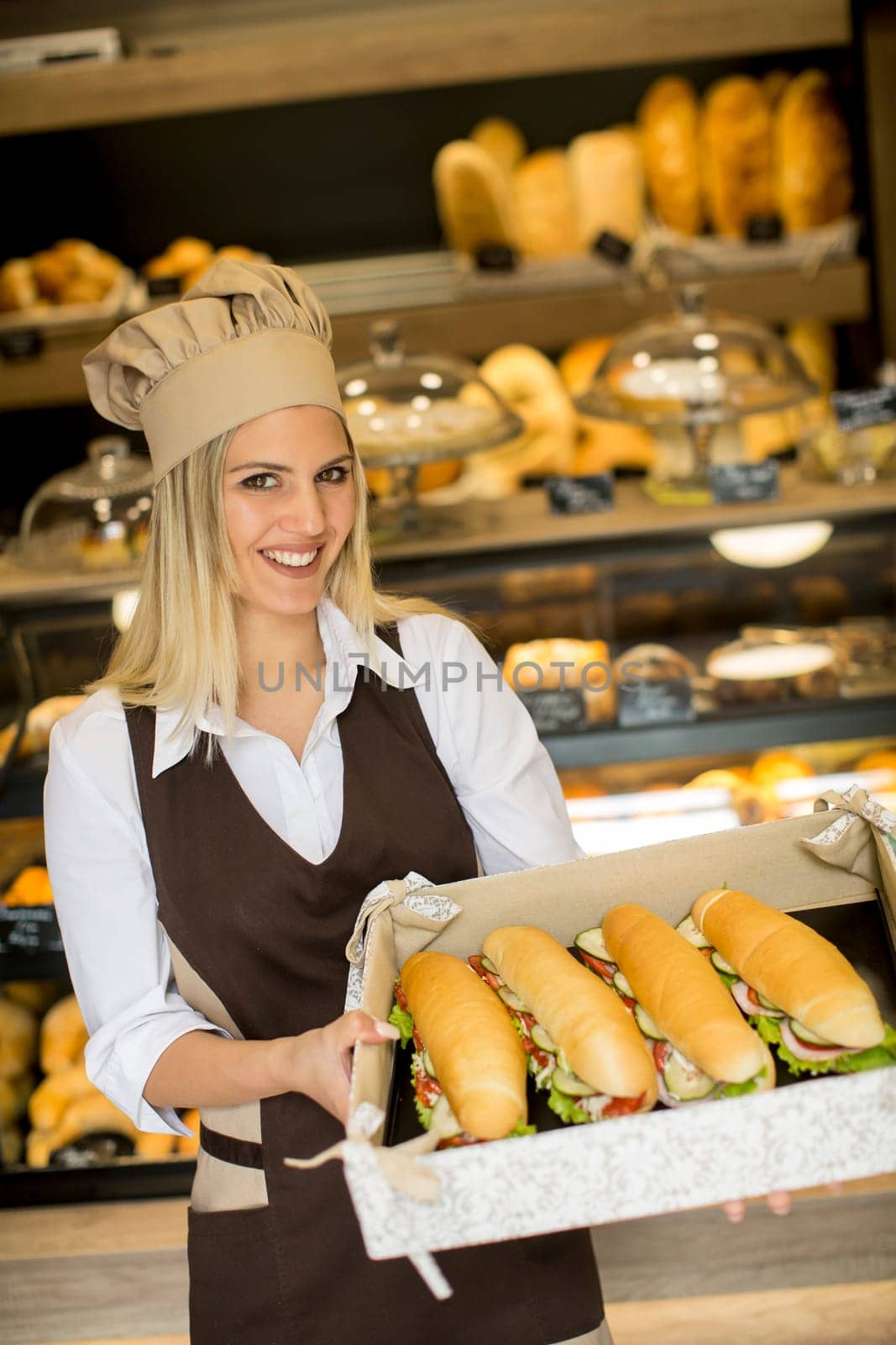 Portrait of female baker posing with various types of sandwiches in the baker shop