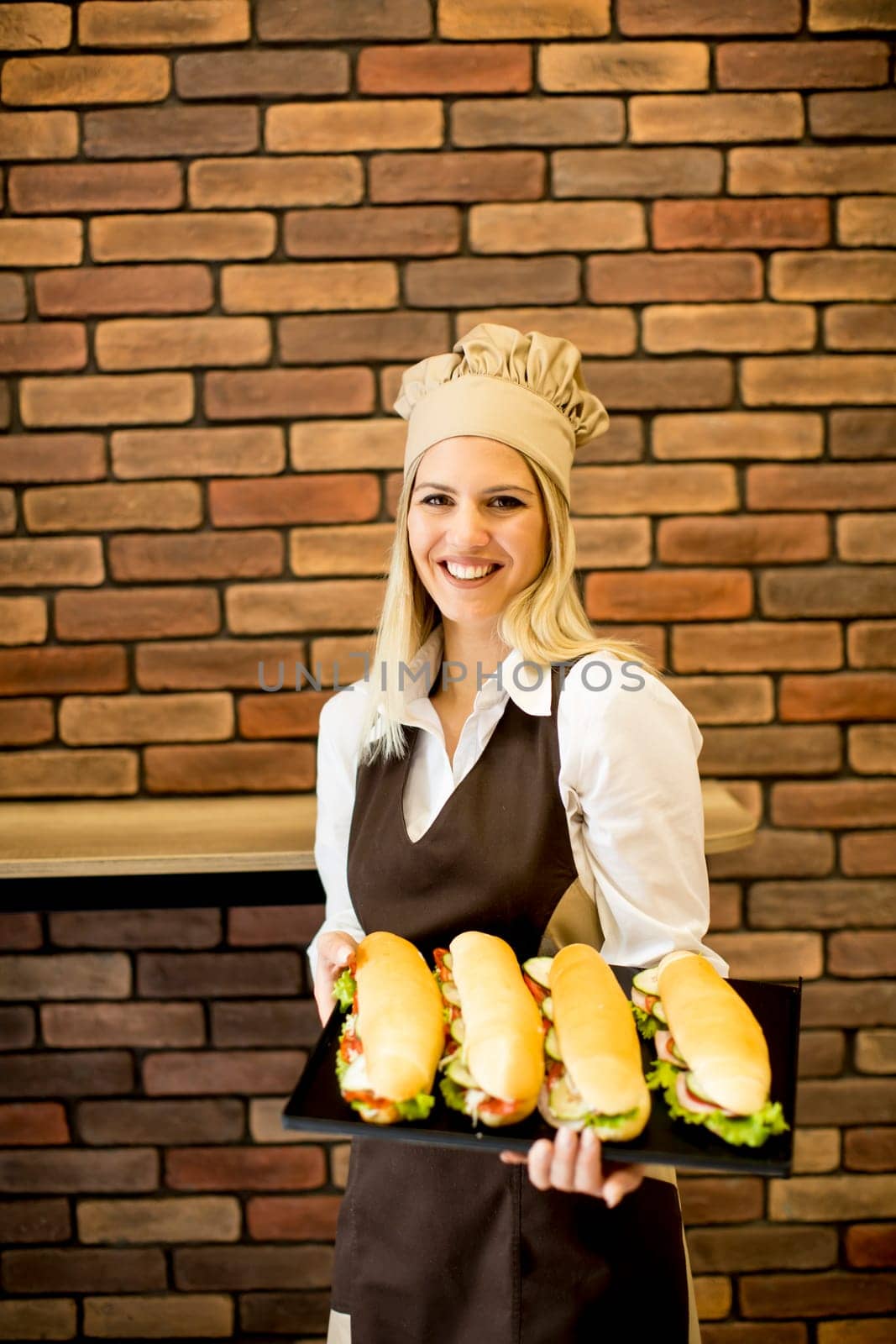 Beautiful female bakery posing with various types of sandwiches in the bakery shop