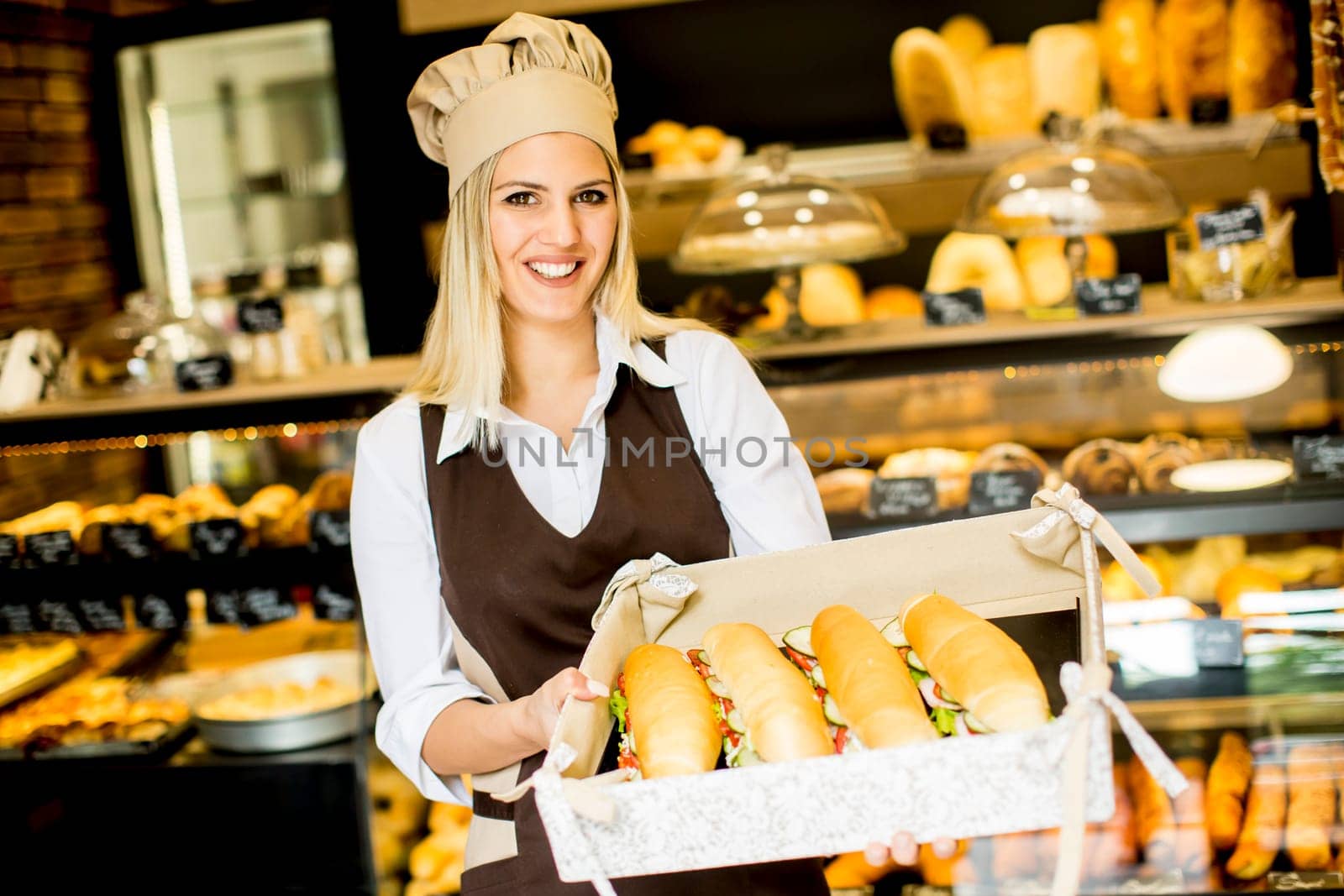Beautiful female bakery posing with various types of sandwiches in the baker shop