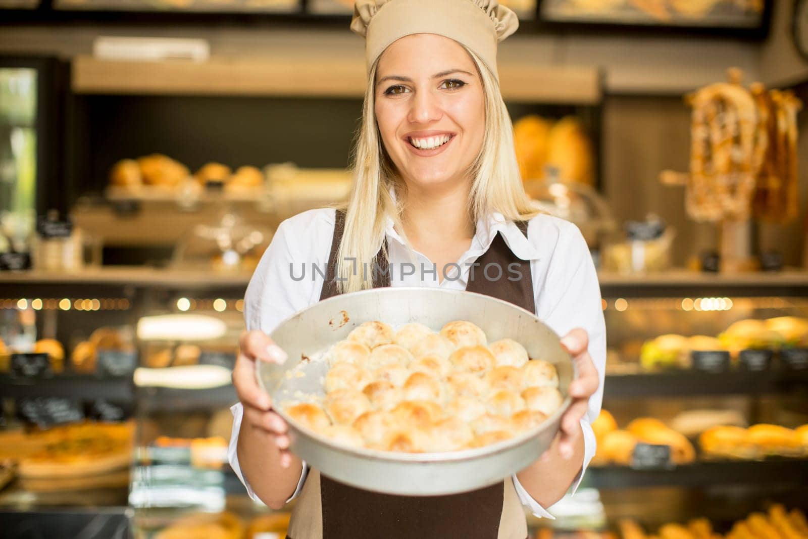 Young woman who works in a bakery posing with a casserole in which the pastry