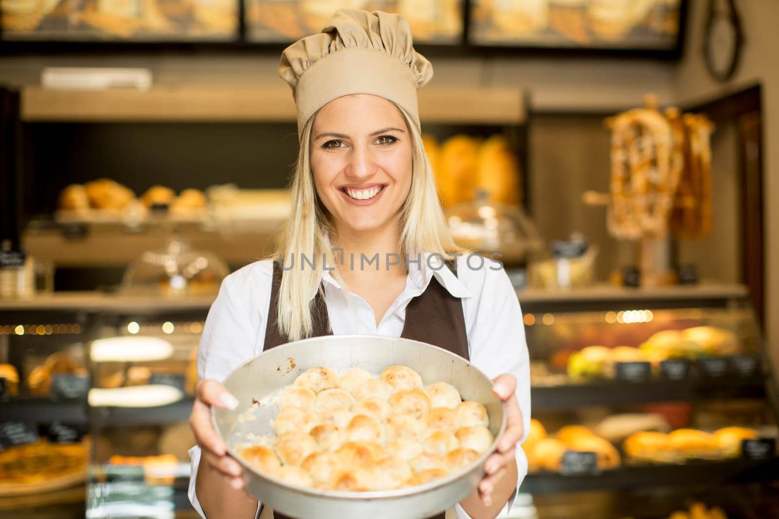 Young woman who works in a bakery posing with a casserole in which the pastry