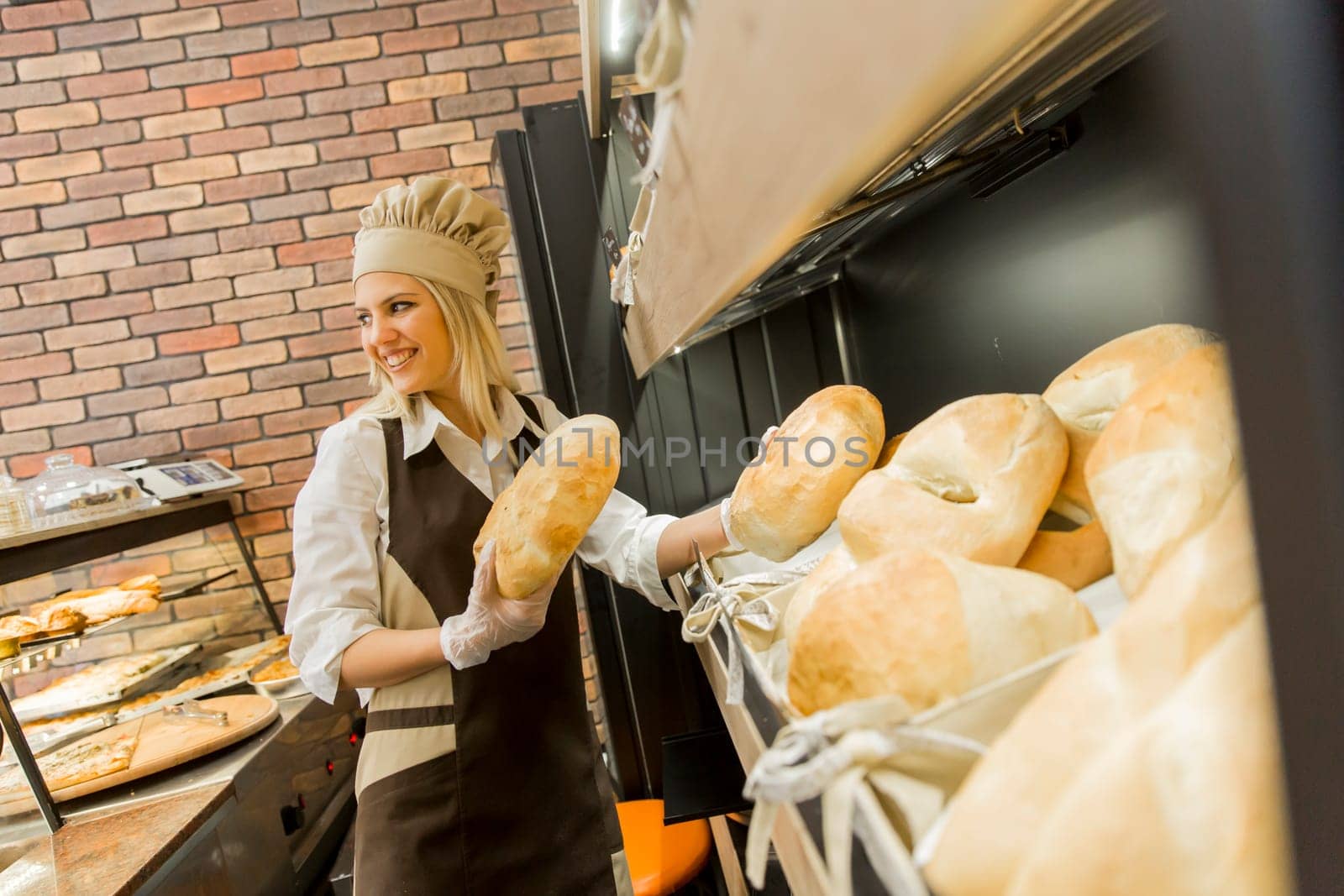 Young woman takes fresh bread from the shelves in a baker shop