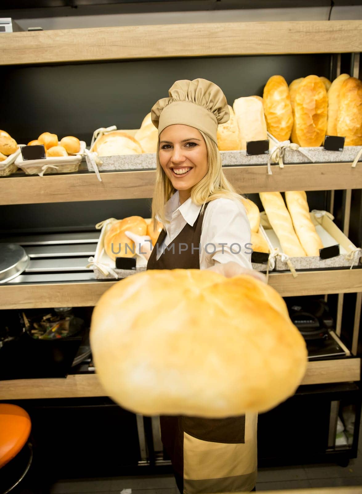 Pretty young woman selling soft  fresh bread in the bakery