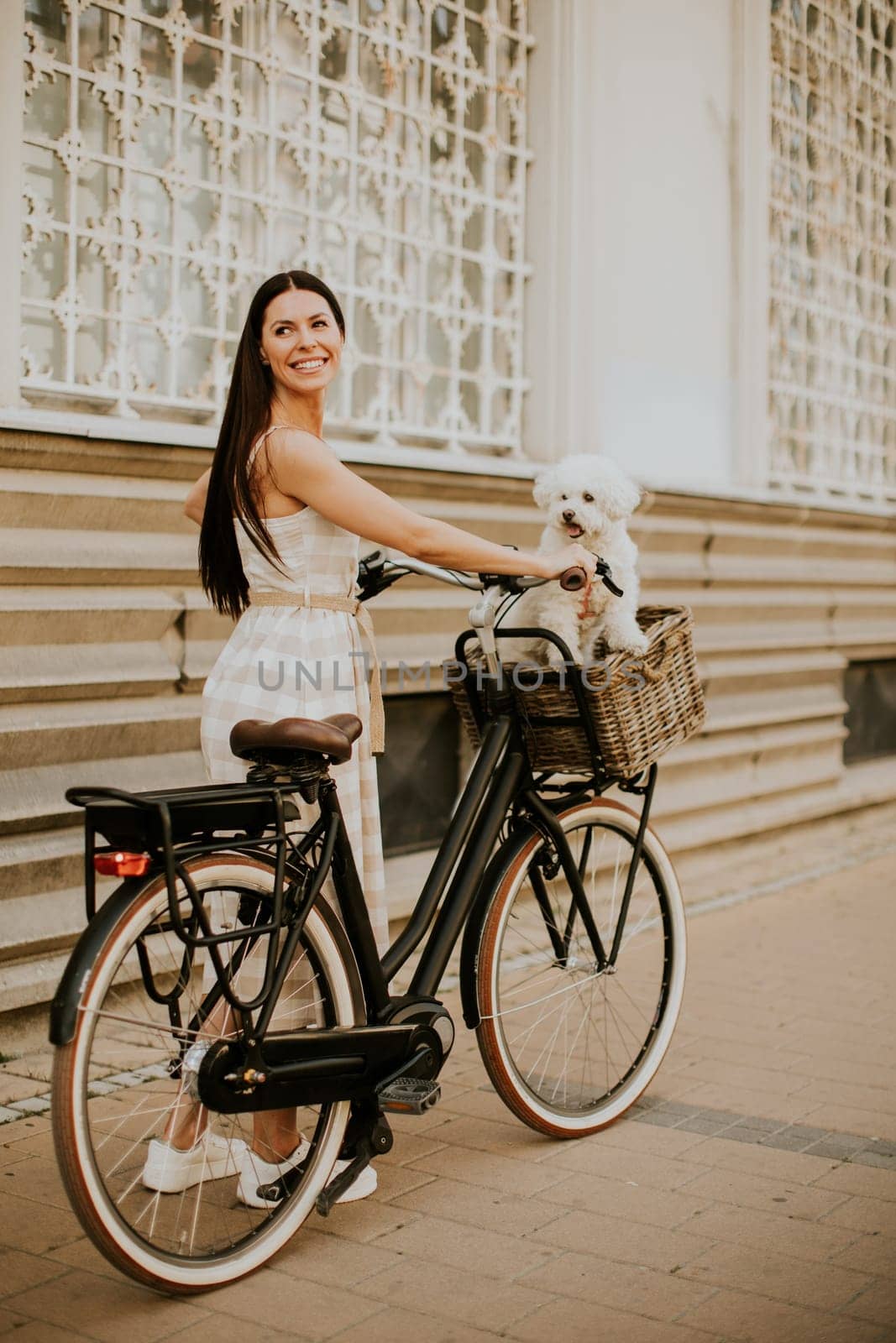 Pretty young woman with white bichon frise dog in the basket of electric bike