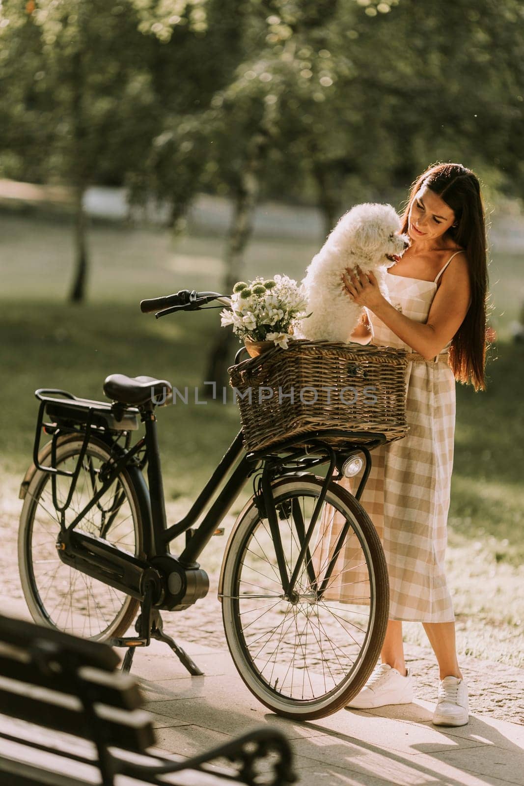 Pretty young woman with white bichon frise dog in the basket of electric bike