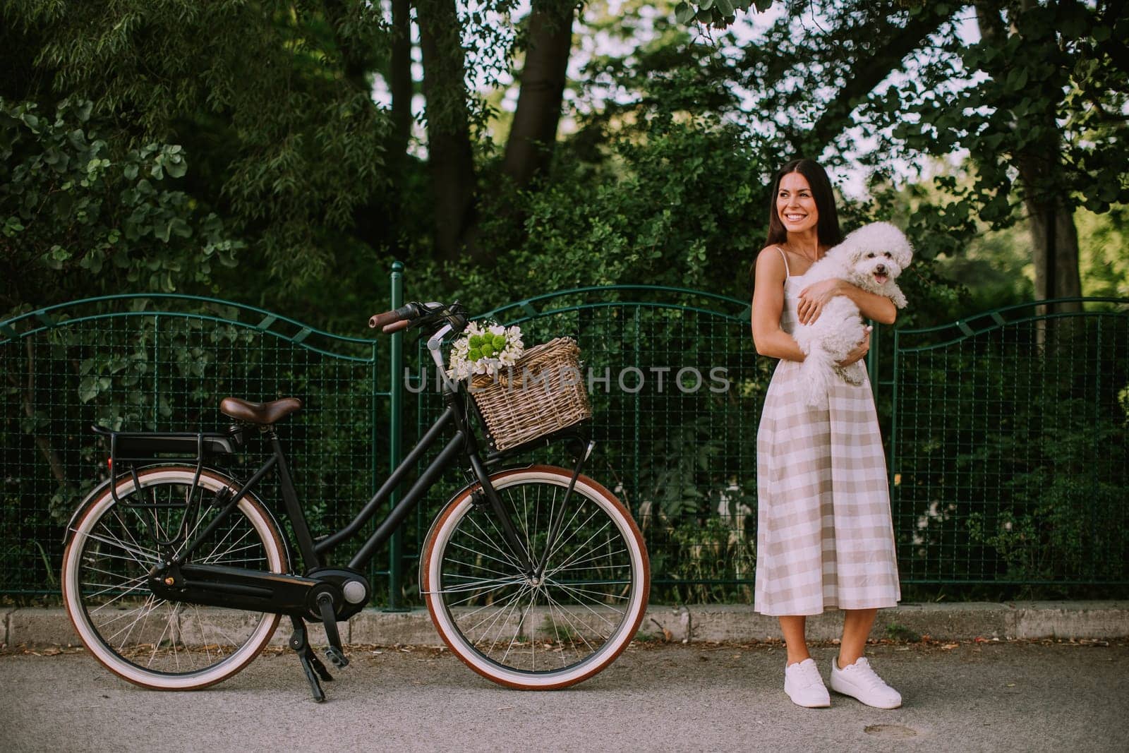 Pretty young woman putting white bichon frise dog in the basket of electric bike