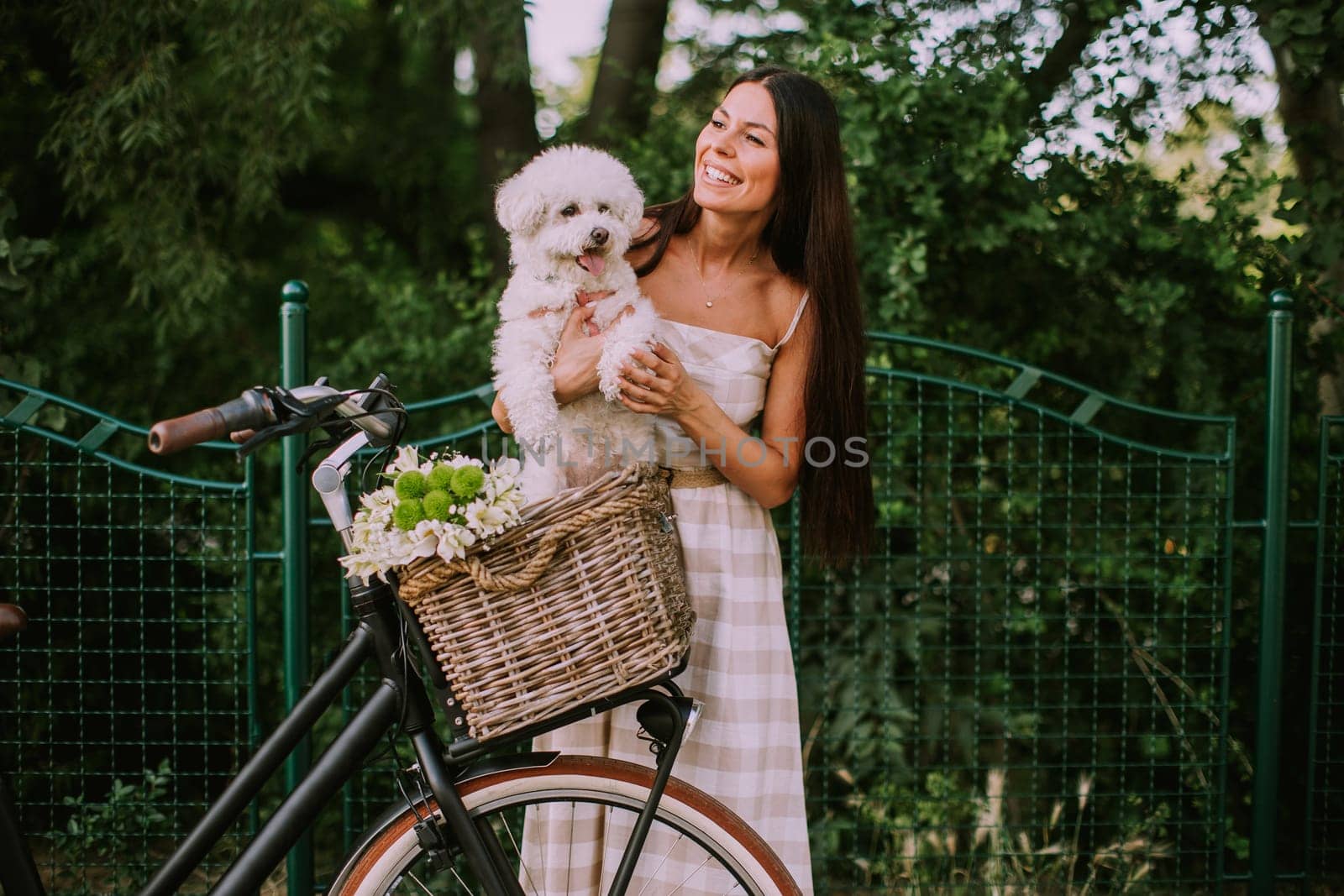 Pretty young woman with white bichon frise dog in the basket of electric bike