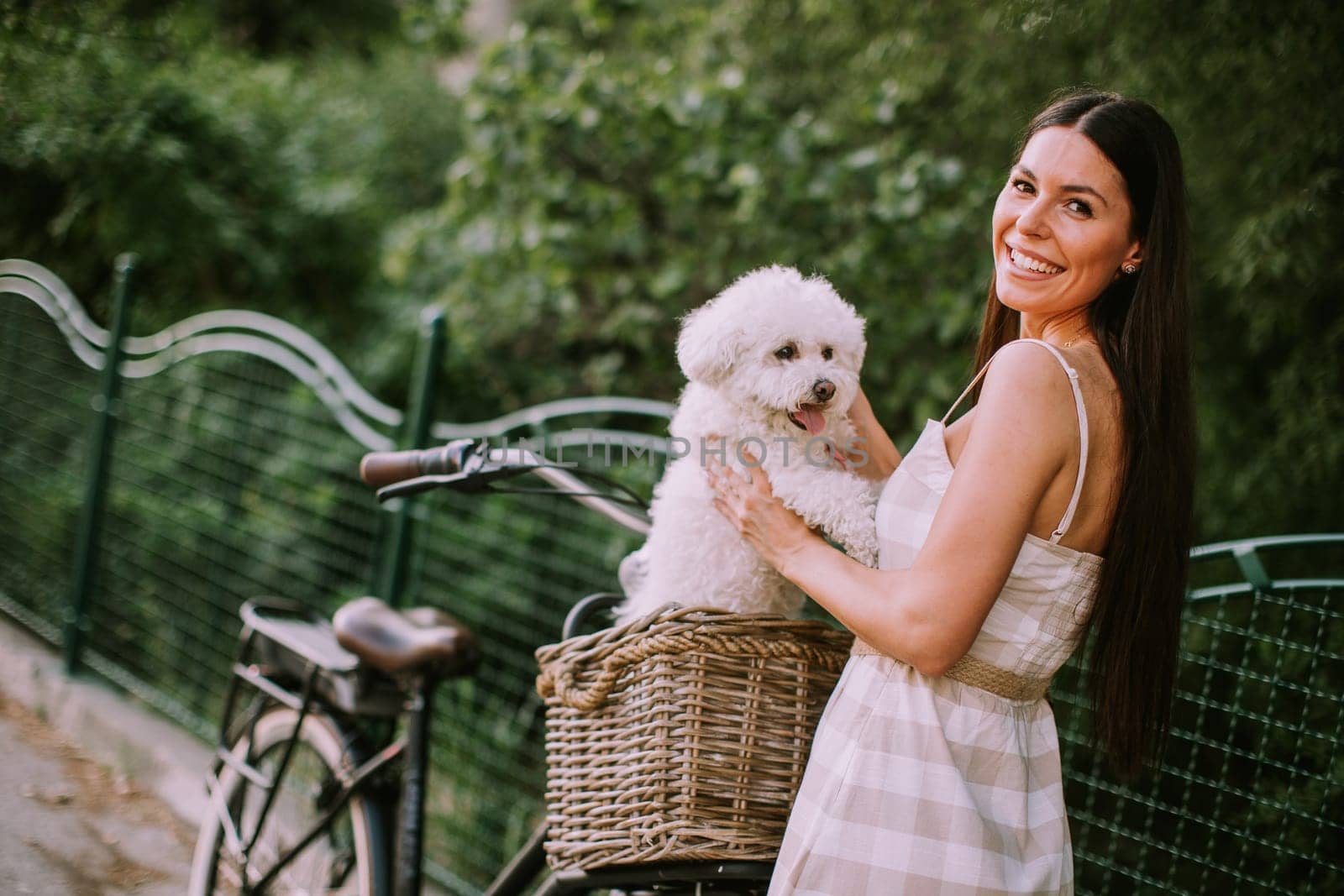 Pretty young woman with white bichon frise dog in the basket of electric bike