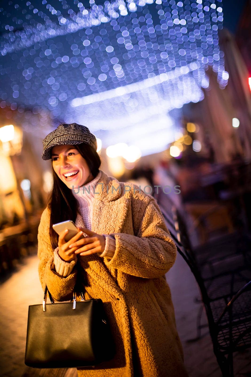 Beautiful young woman using her mobile phone in the street at Christmas time