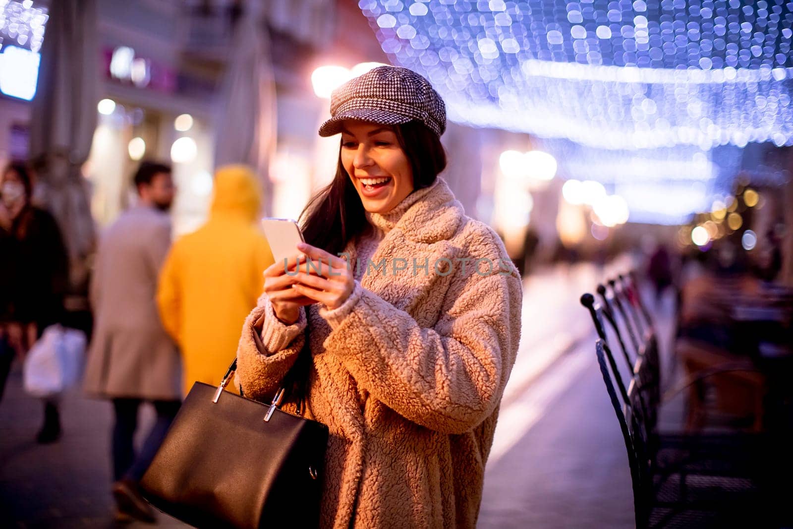 Beautiful young woman using her mobile phone in the street at Christmas time