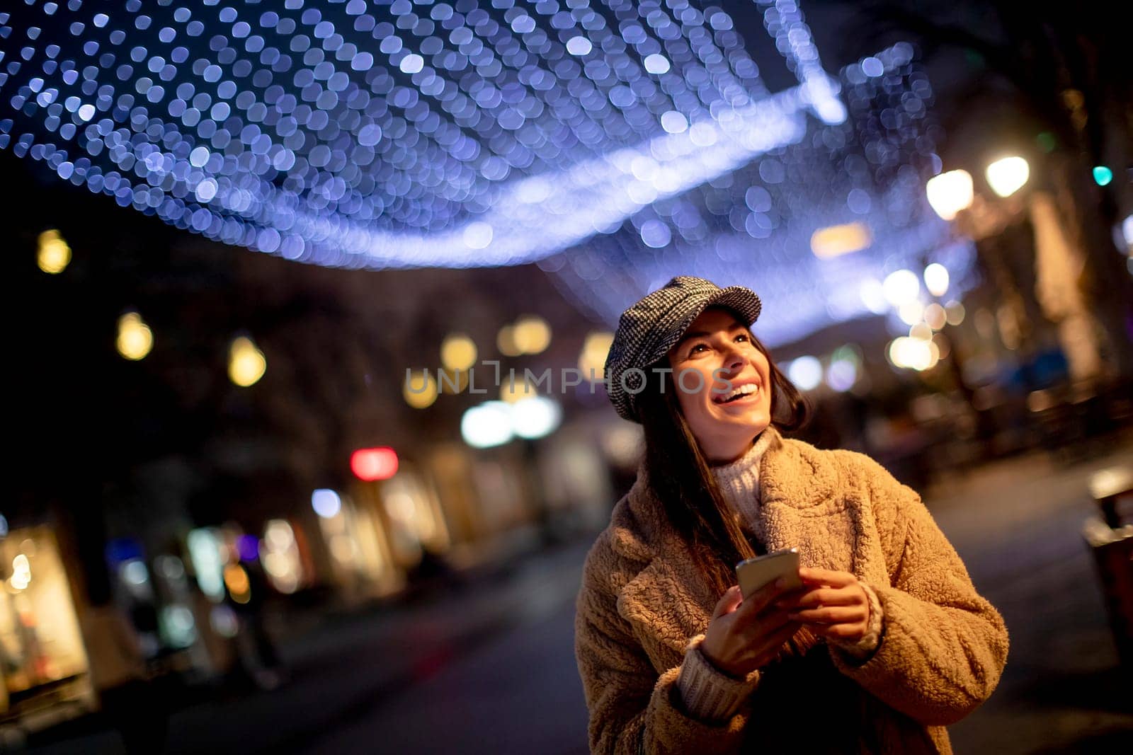 Beautiful young woman using her mobile phone in the street at Christmas time