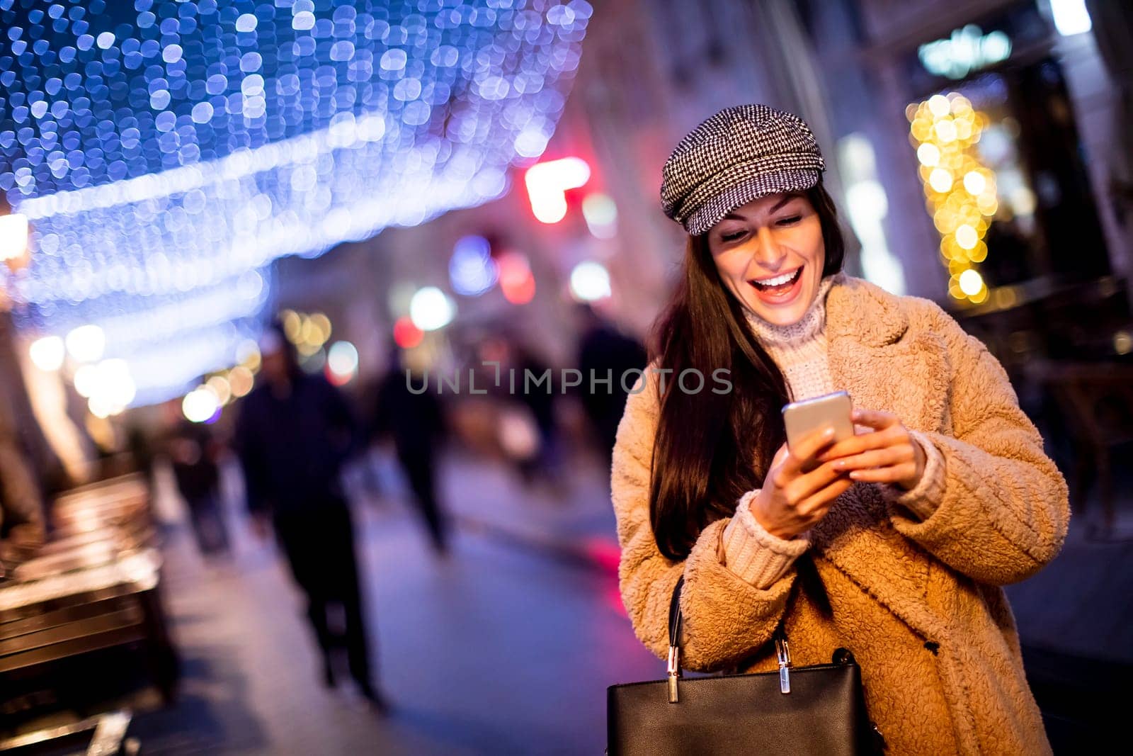 Beautiful young woman using her mobile phone in the street at Christmas time