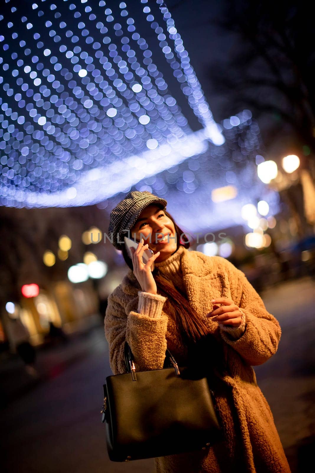 Beautiful young woman using her mobile phone in the street at Christmas time