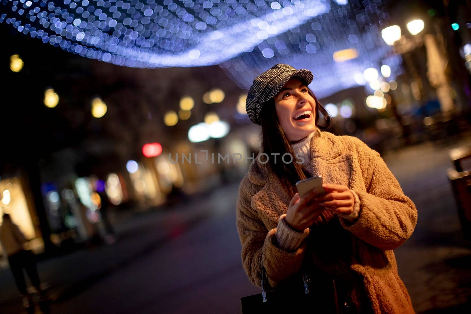 Beautiful young woman using her mobile phone in the street at Christmas time