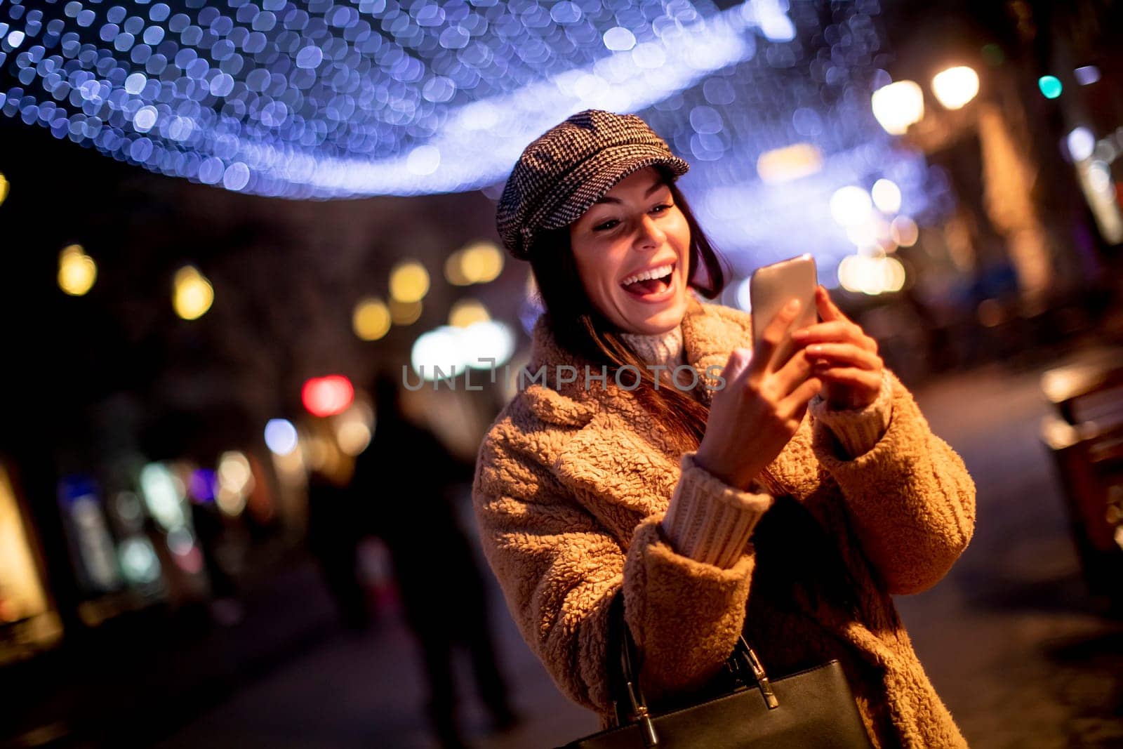Beautiful young woman using her mobile phone in the street at Christmas time