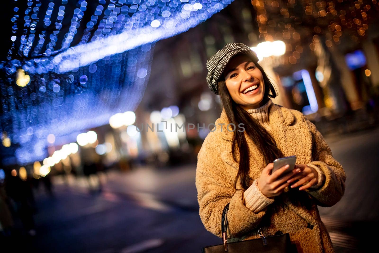 Beautiful young woman using her mobile phone in the street at Christmas time