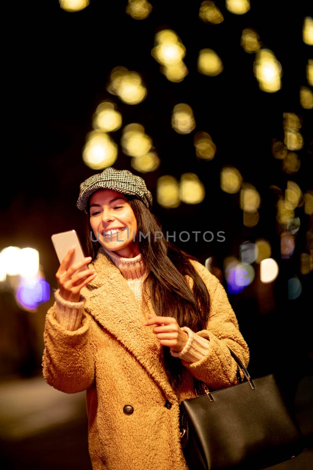 Beautiful young woman using her mobile phone in the street at Christmas time