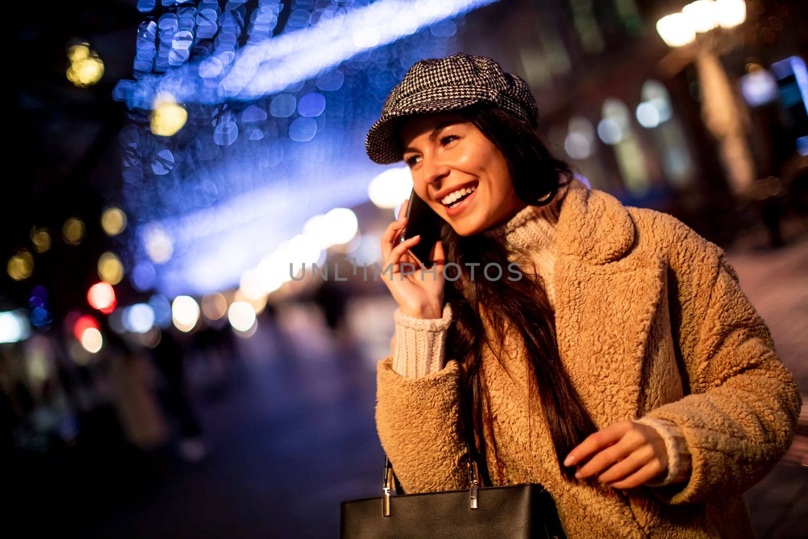 Beautiful young woman using her mobile phone in the street at Christmas time