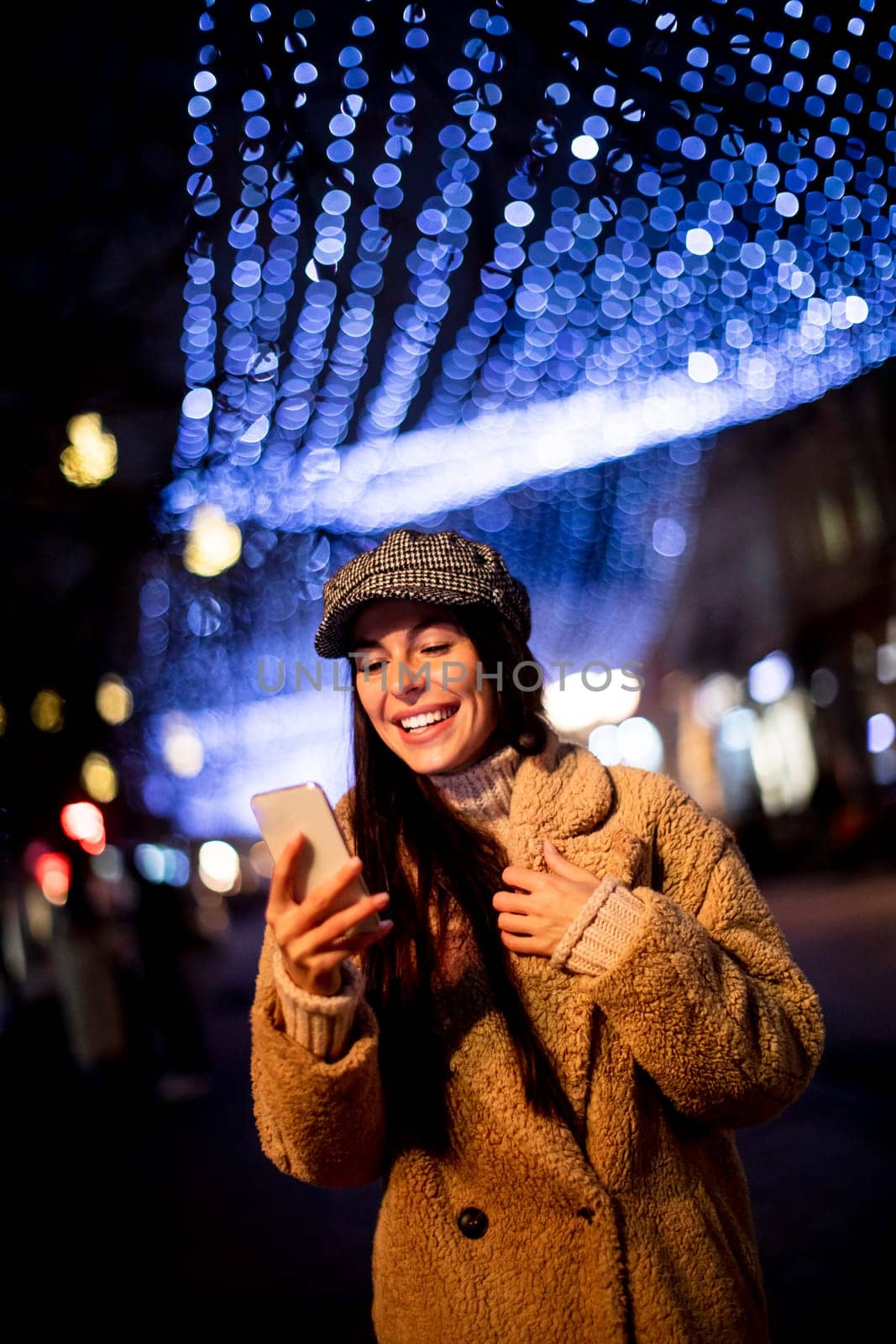 Beautiful young woman using her mobile phone in the street at Christmas time