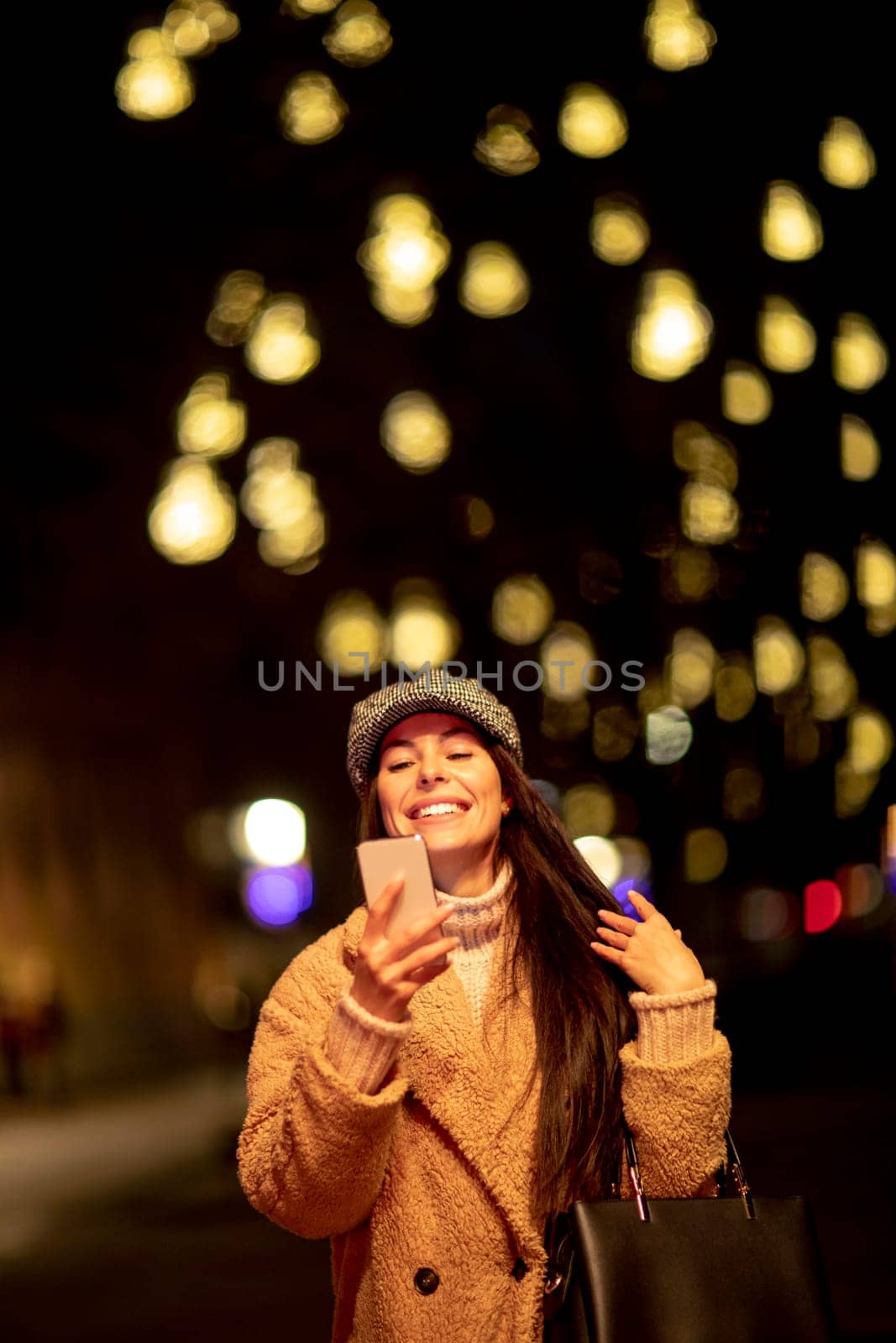 Beautiful young woman using her mobile phone in the street at Christmas time