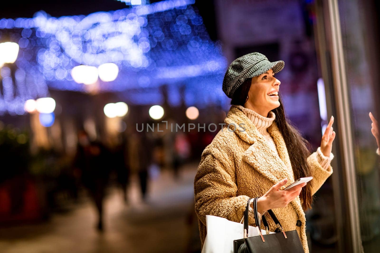Pretty young woman with mobile phone by the shop window at Christmas time