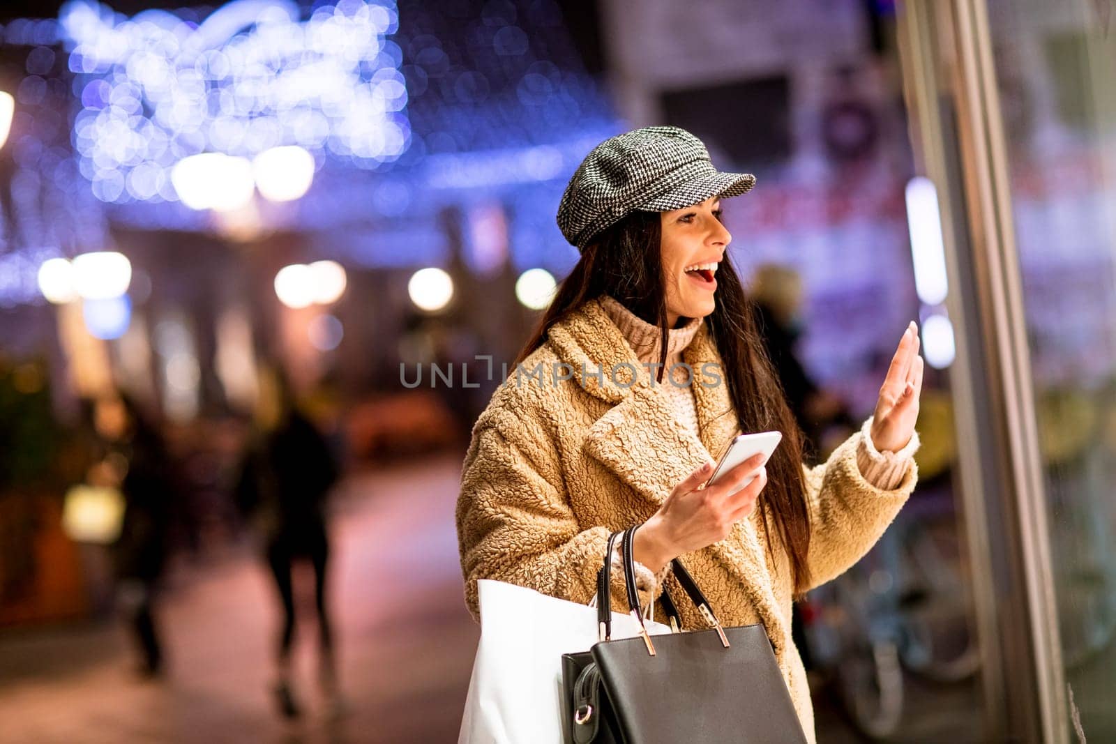 Pretty young woman with mobile phone by the shop window at Christmas time