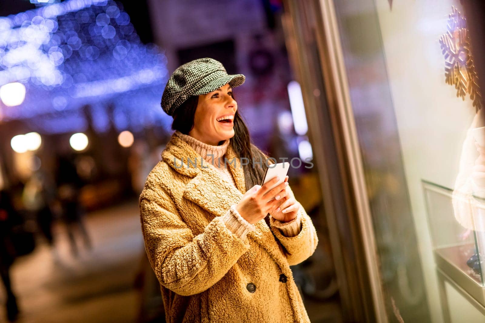 Pretty young woman with mobile phone by the shop window at Christmas time