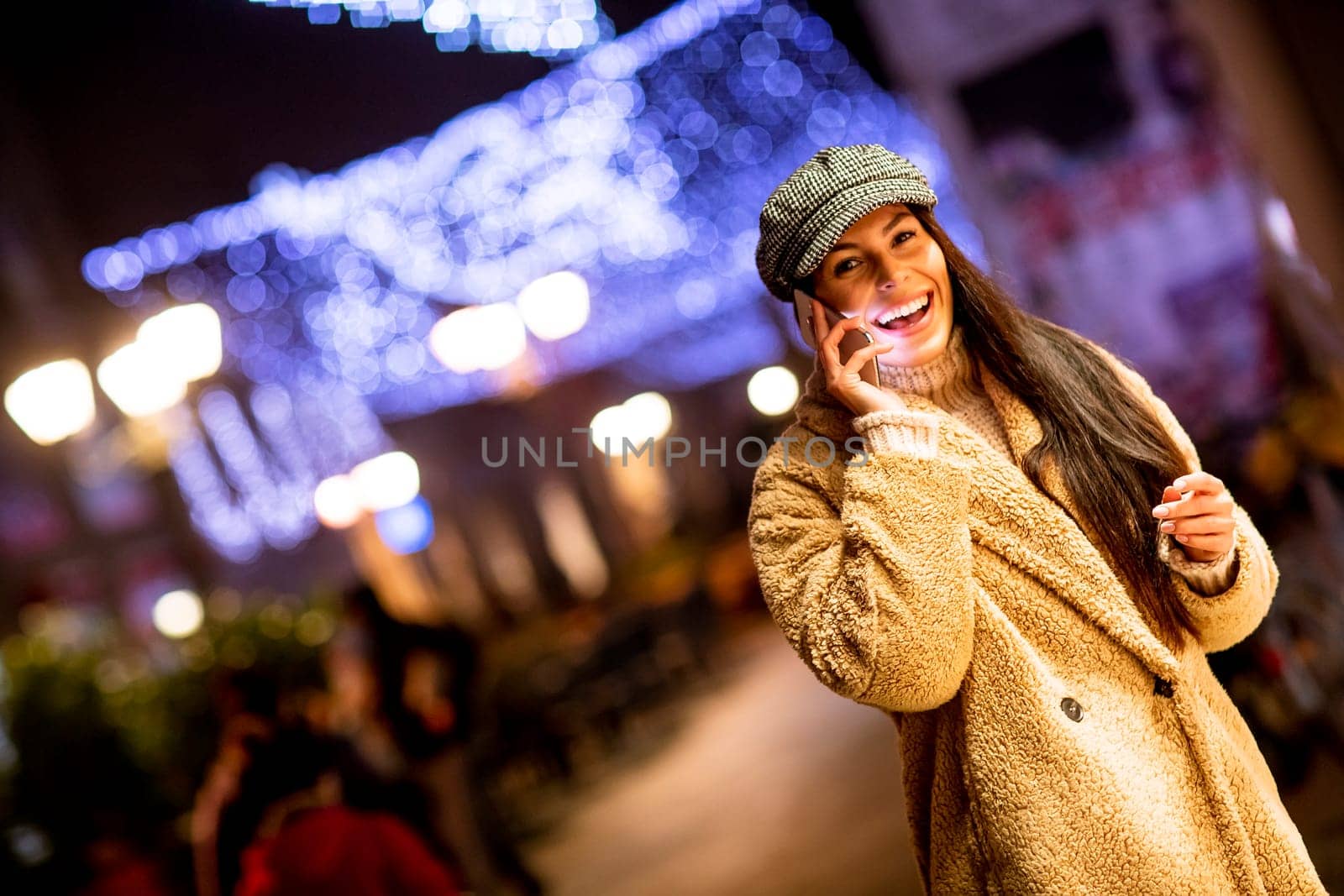 Beautiful young woman using her mobile phone in the street at Christmas time