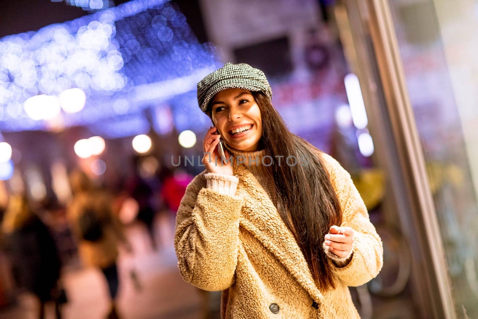 Beautiful young woman using her mobile phone in the street at Christmas time