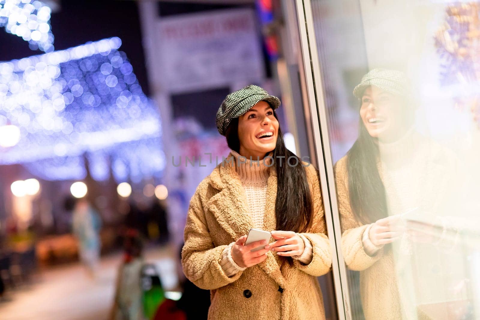 Pretty young woman with mobile phone by the shop window at Christmas time