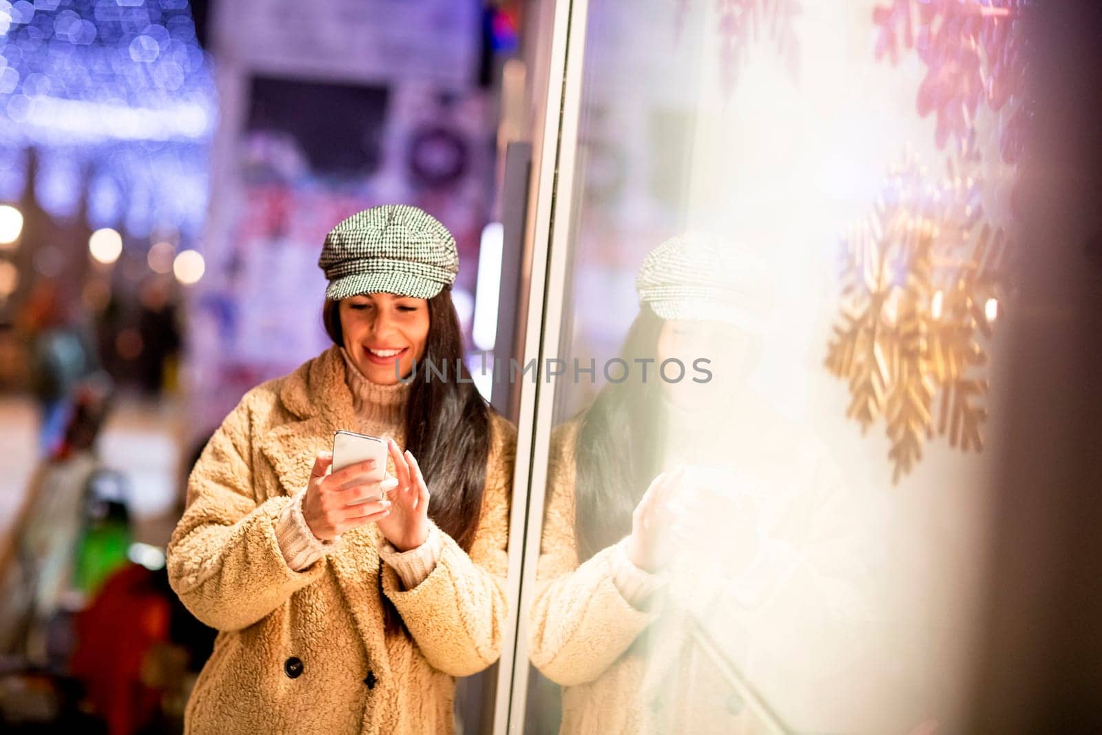 Pretty young woman with mobile phone by the shop window at Christmas time