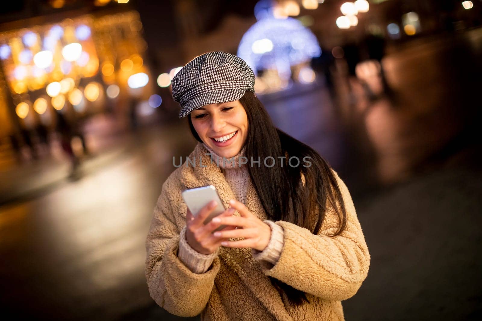Beautiful young woman using her mobile phone in the street at Christmas time