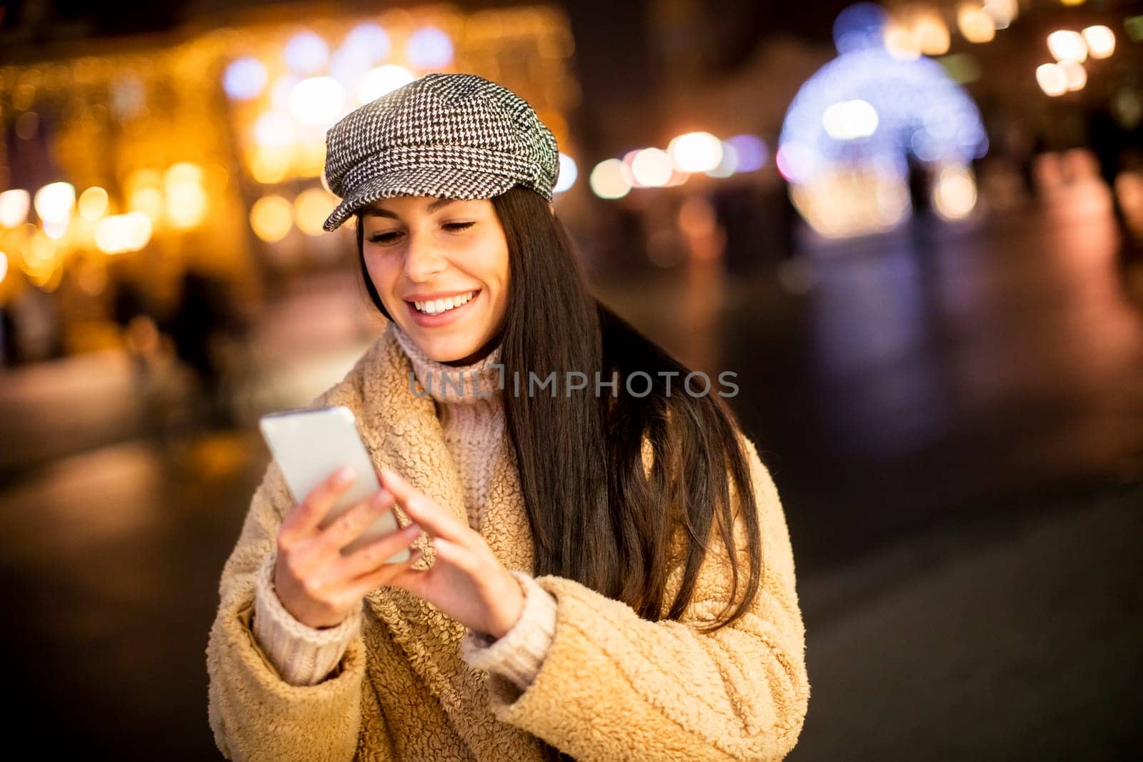 Beautiful young woman using her mobile phone in the street at Christmas time