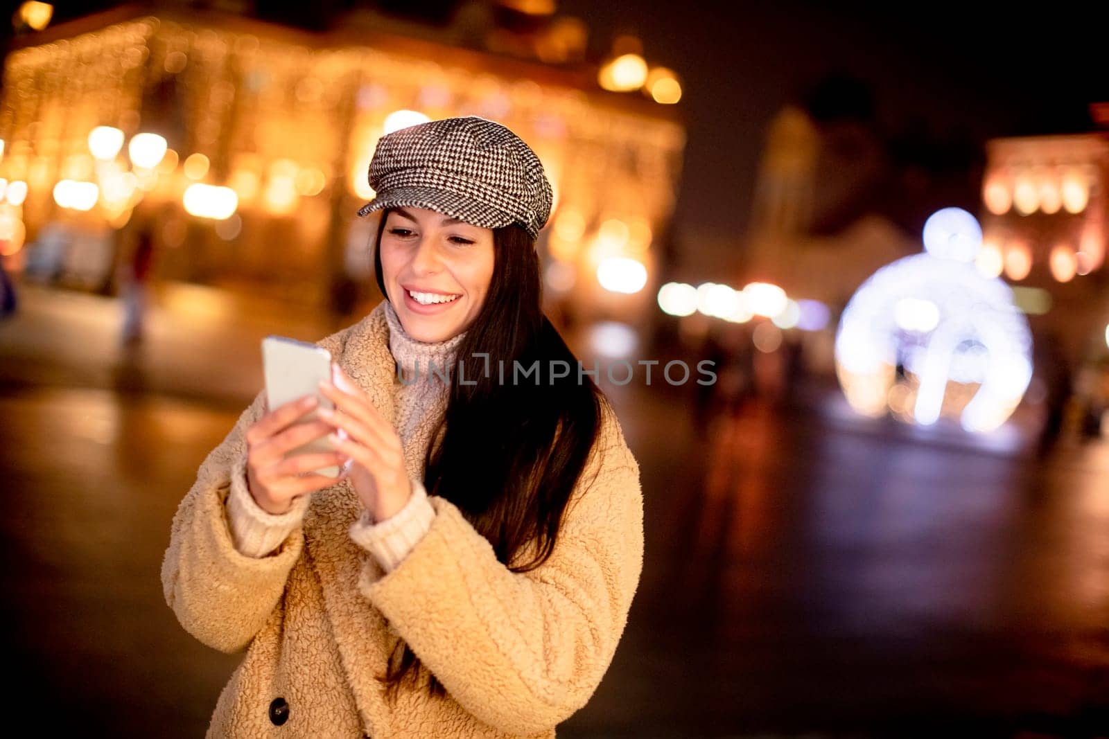 Beautiful young woman using her mobile phone in the street at Christmas time