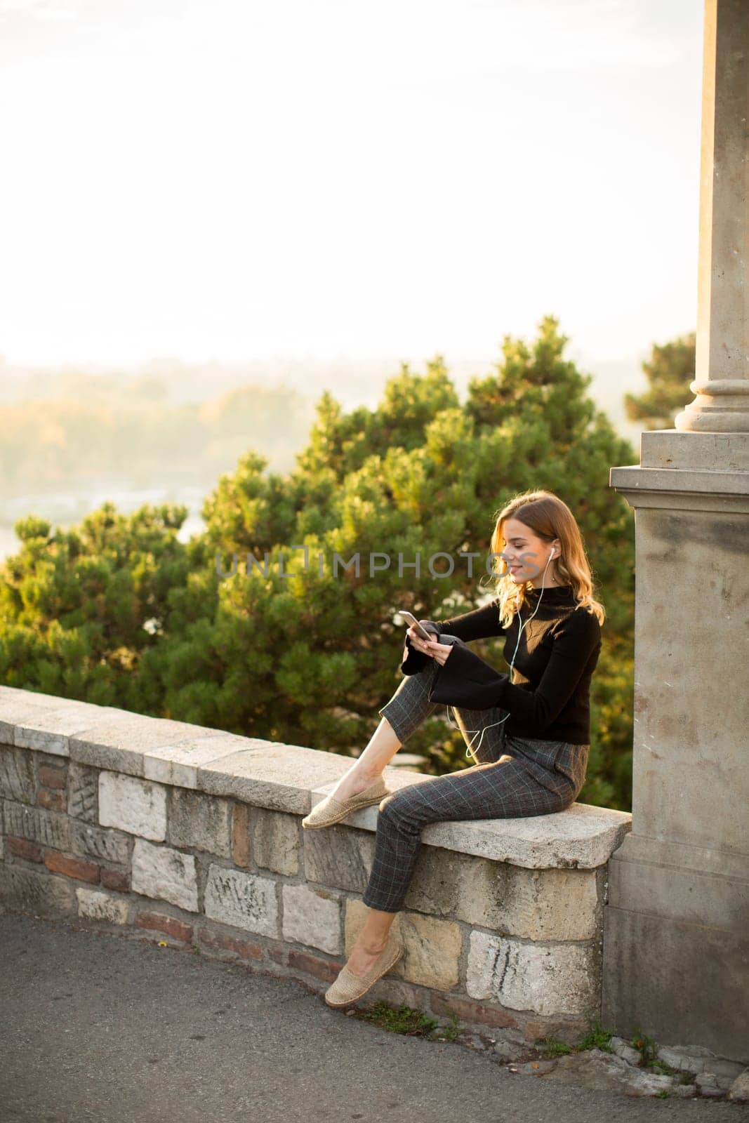 Portrait of young woman holding mobile phone while sitting on the wall