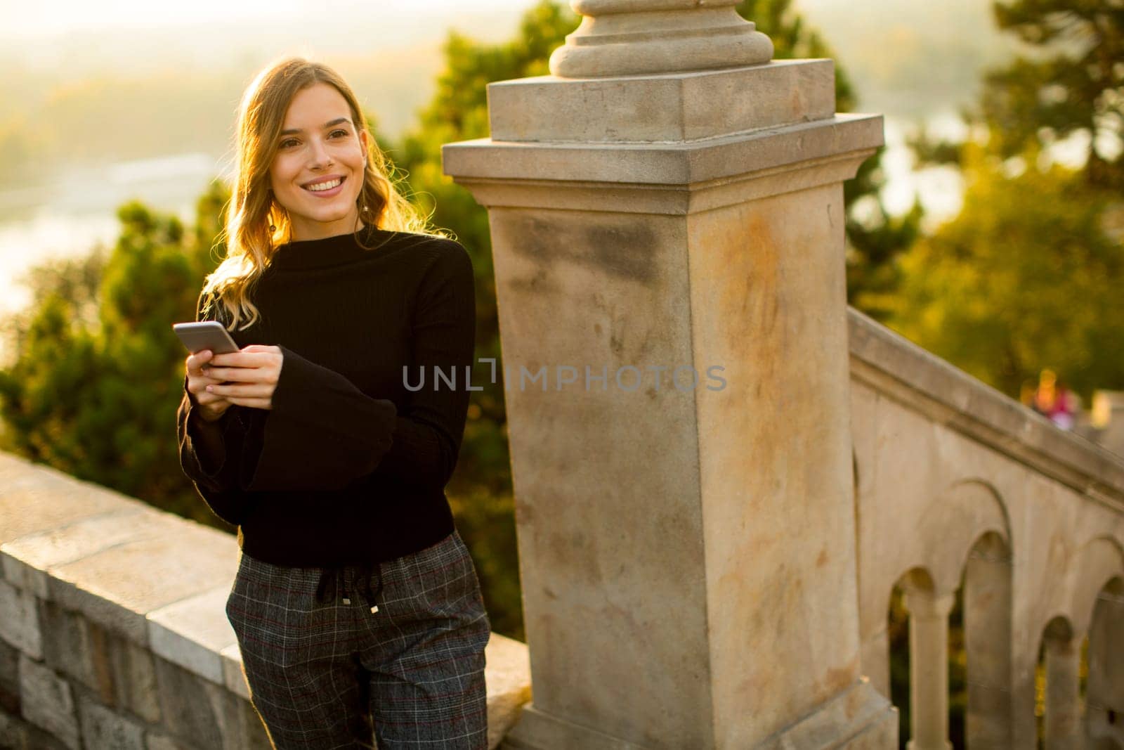 Portrait of young woman holding mobile phone while standing on the old stairs in the park