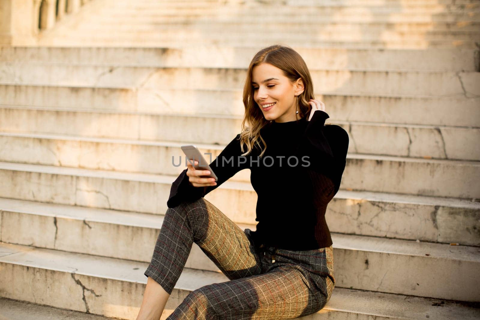 Trendy young woman with mobile phone sitting at stairs outdoor
