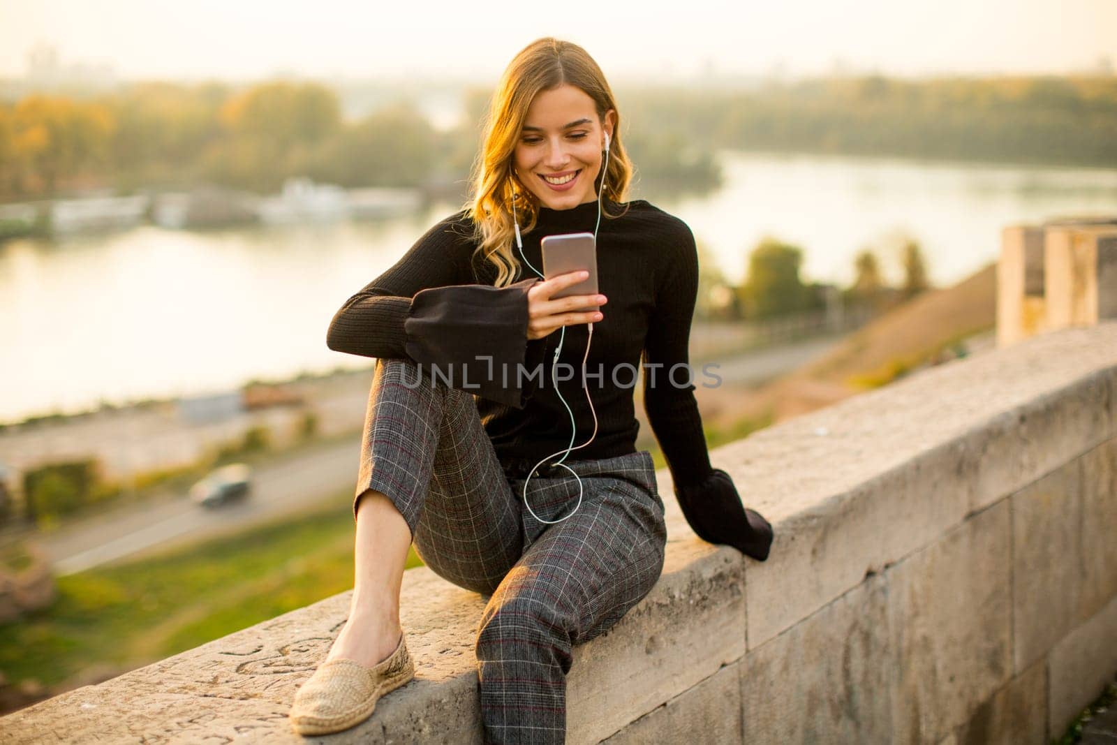 Trendy young woman listening music from smartphone outdoor at sunset