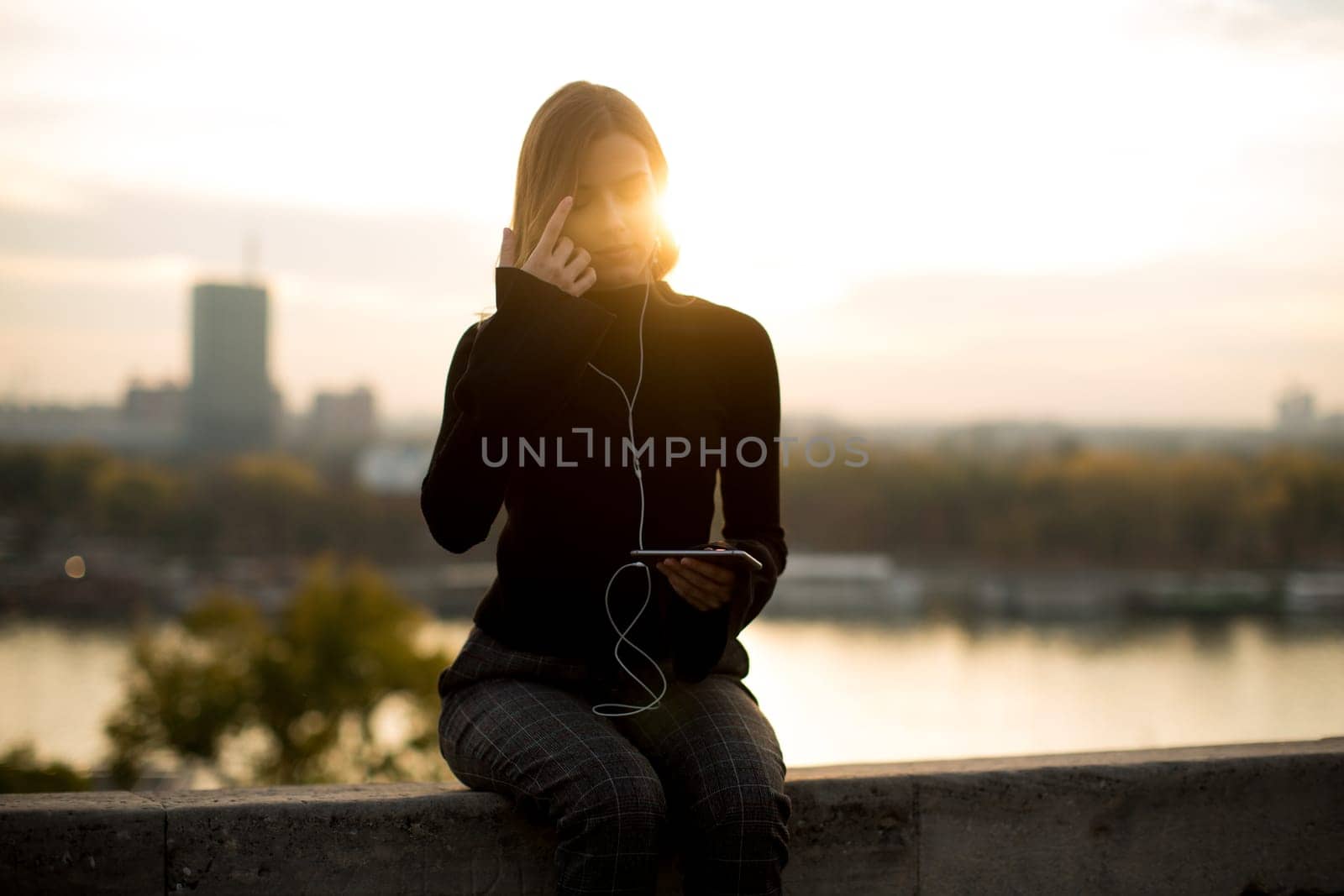 Portrait of trendy young woman listening music from smartphone outdoor at sunset