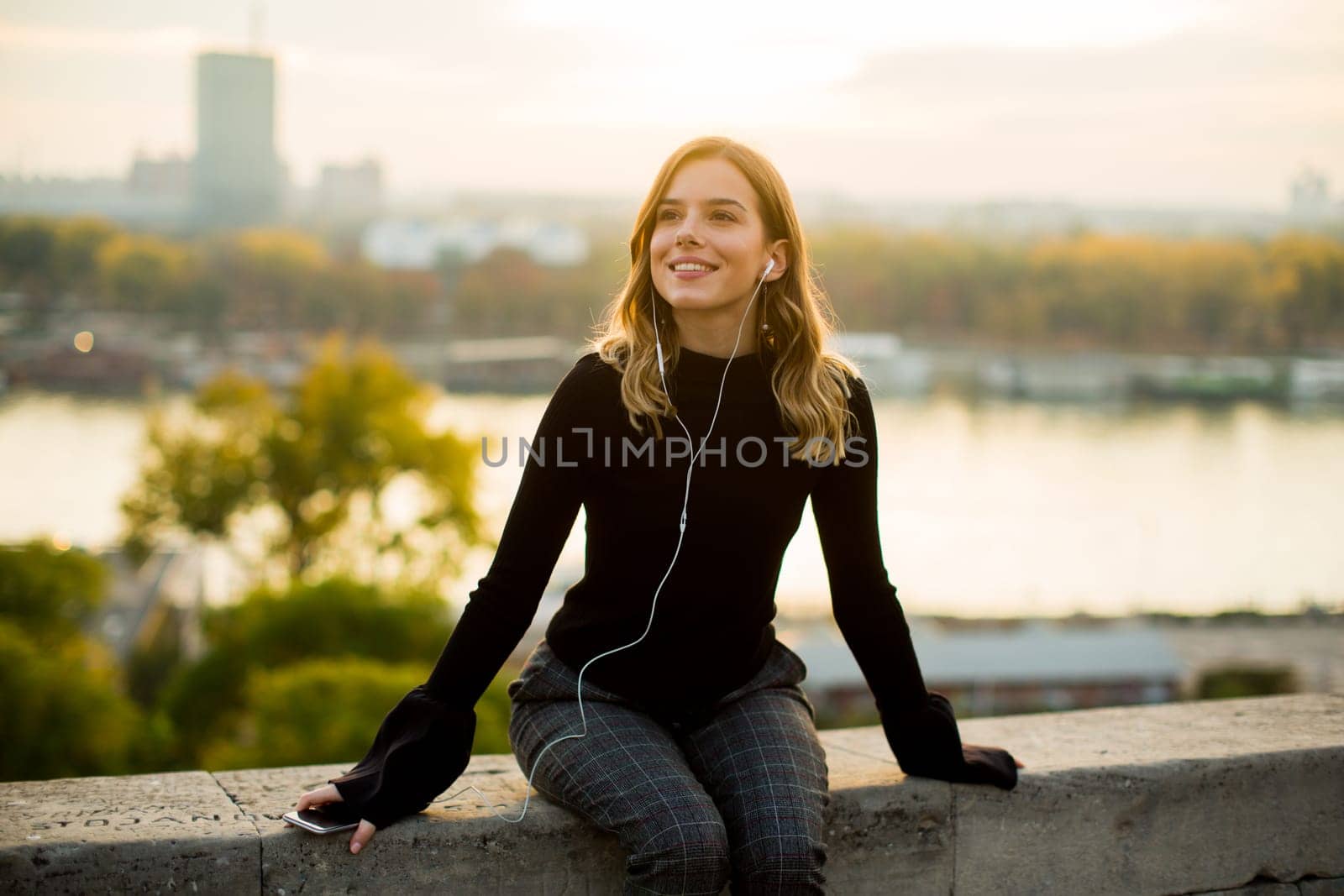 Portrait of trendy young woman listening music from smartphone outdoor at sunset