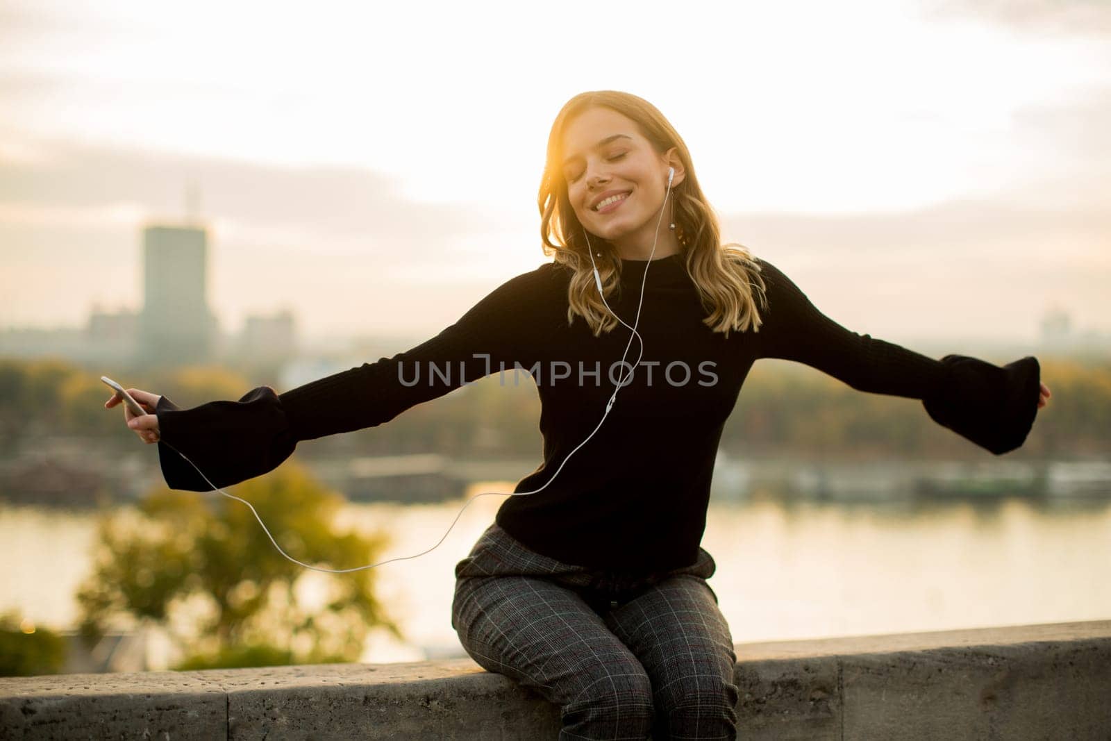 Trendy young woman listening music from smartphone outdoor at sunset