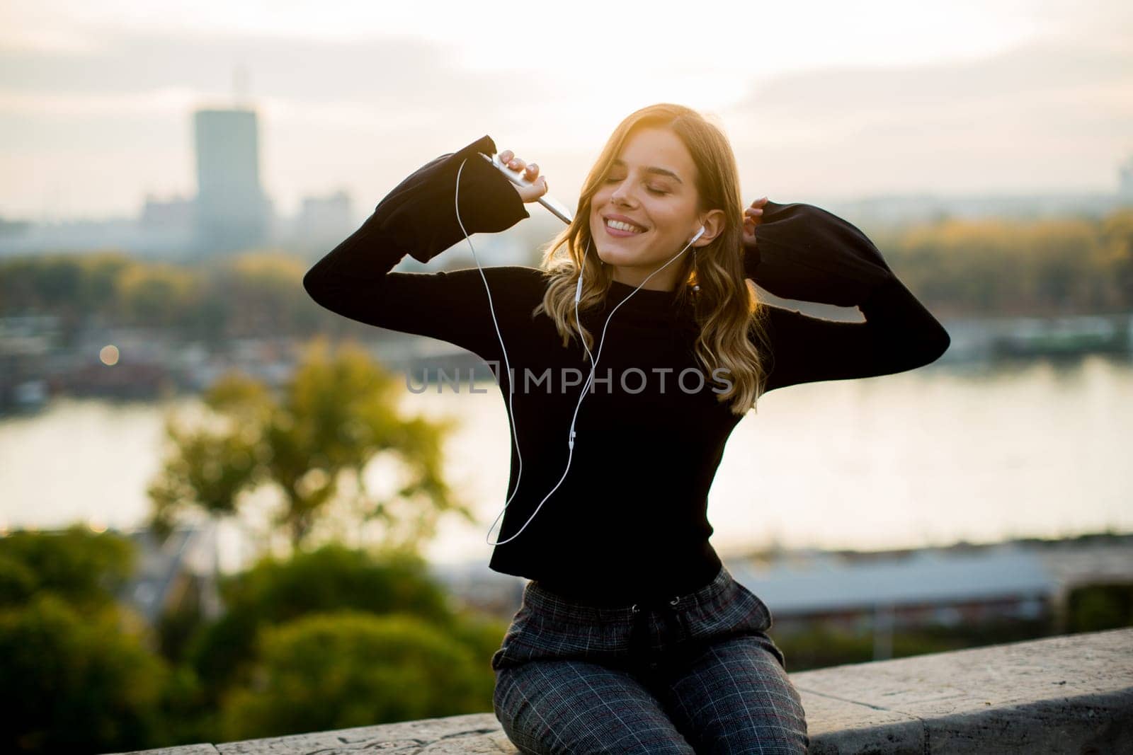 Trendy young woman listening music from smartphone outdoor at sunset